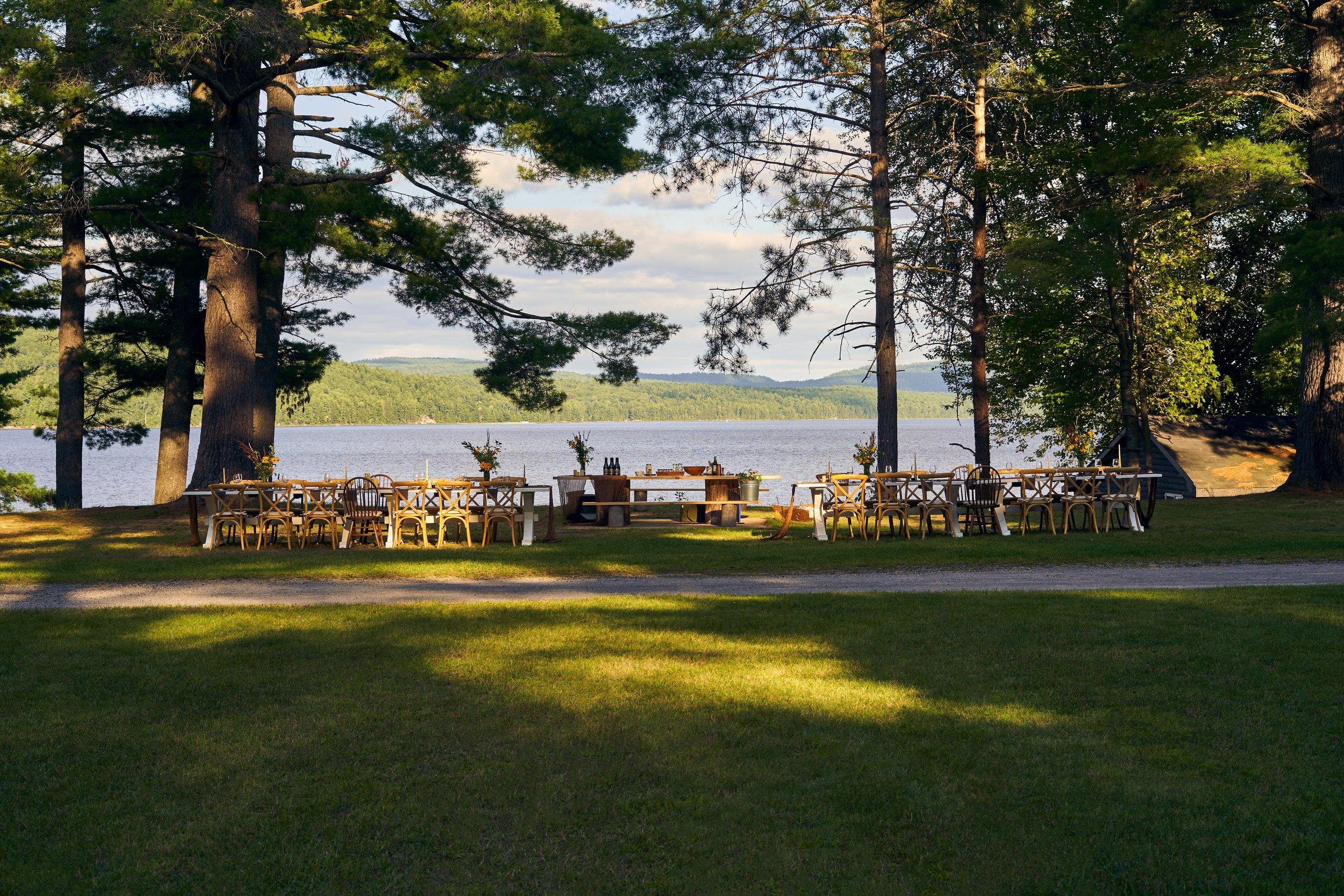 The Wild Path Dinner at Anupaya setup with wooden chairs and tables, surrounded by tall trees, overlooking a calm lake  Photographed for the Perch Cookbook by Gumption Studio, Ottawa Cookbook photographer.