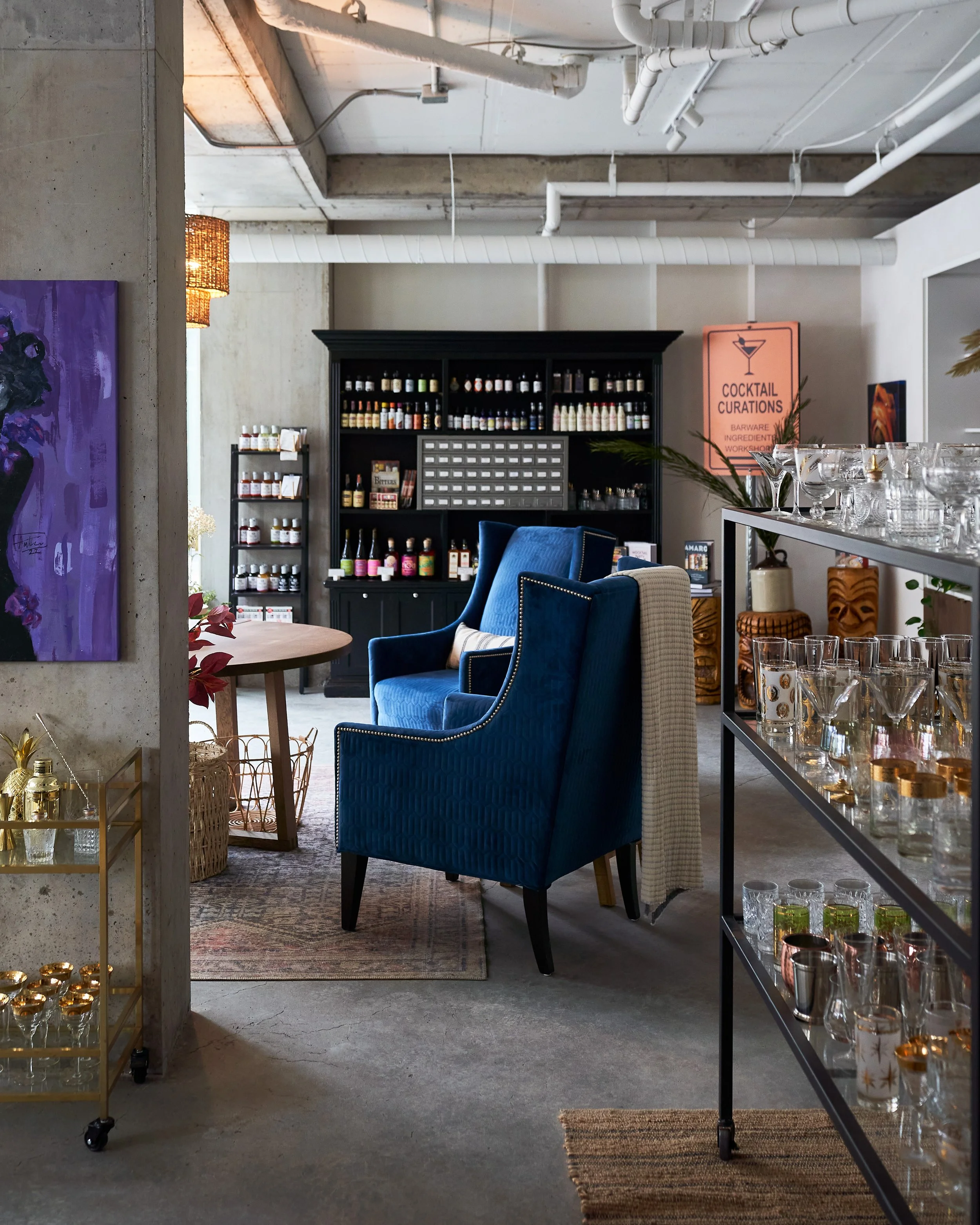 Interior of Split Tree with glassware and bottles displayed on shelves, a blue armchair, and side table. Photographed by Gumption Studio, Ottawa interior photographer.