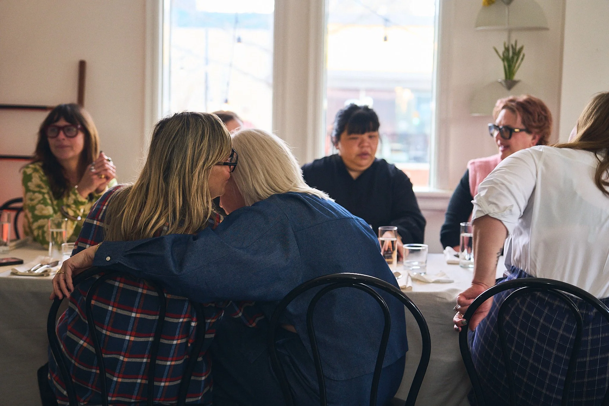 Group of people sitting around a dining table at Girl Dinner at Parlour, some laughing and talking. Photographed by Gumption Studio, Ottawa event photographer.