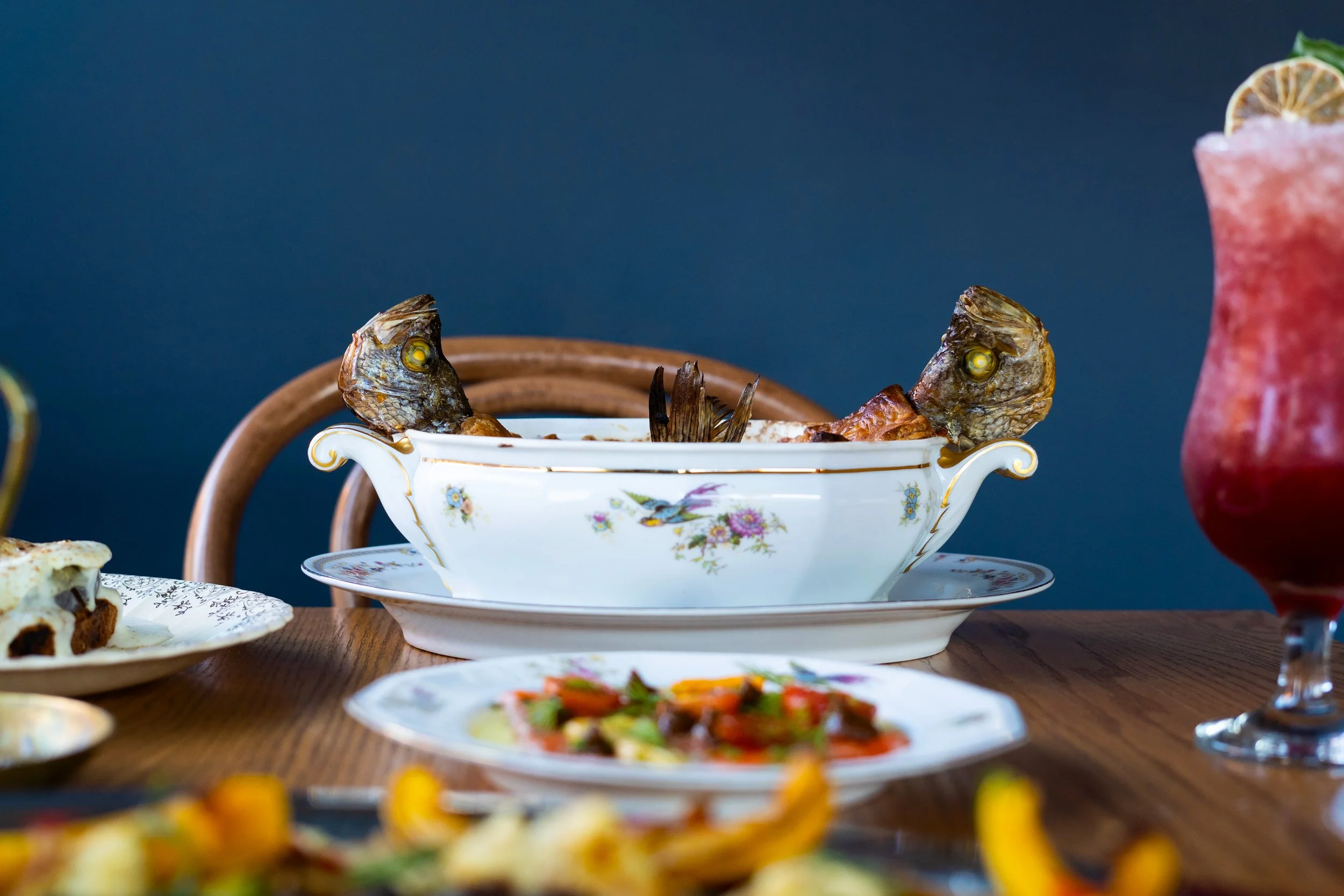 A table with various dishes by Le Poisson Bleu including a porcelain bowl with fish heads. Photographed by Gumption Studio, Ottawa food photographer. 