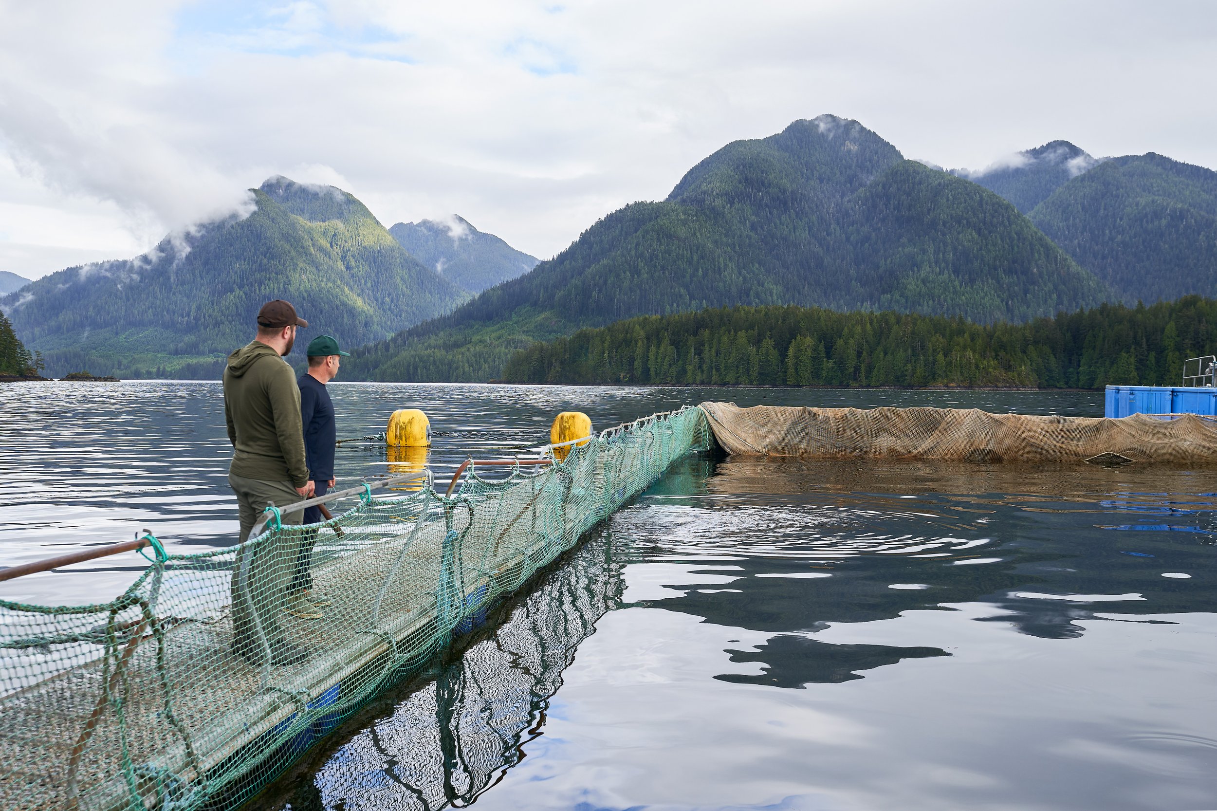 Justin Champagne-Lagarde on a floating dock at Golden Eagle Black Cod, with green mountains and cloudy sky in the background. Photographed for the Perch Cookbook by Gumption Studio, Ottawa Cookbook photographer.