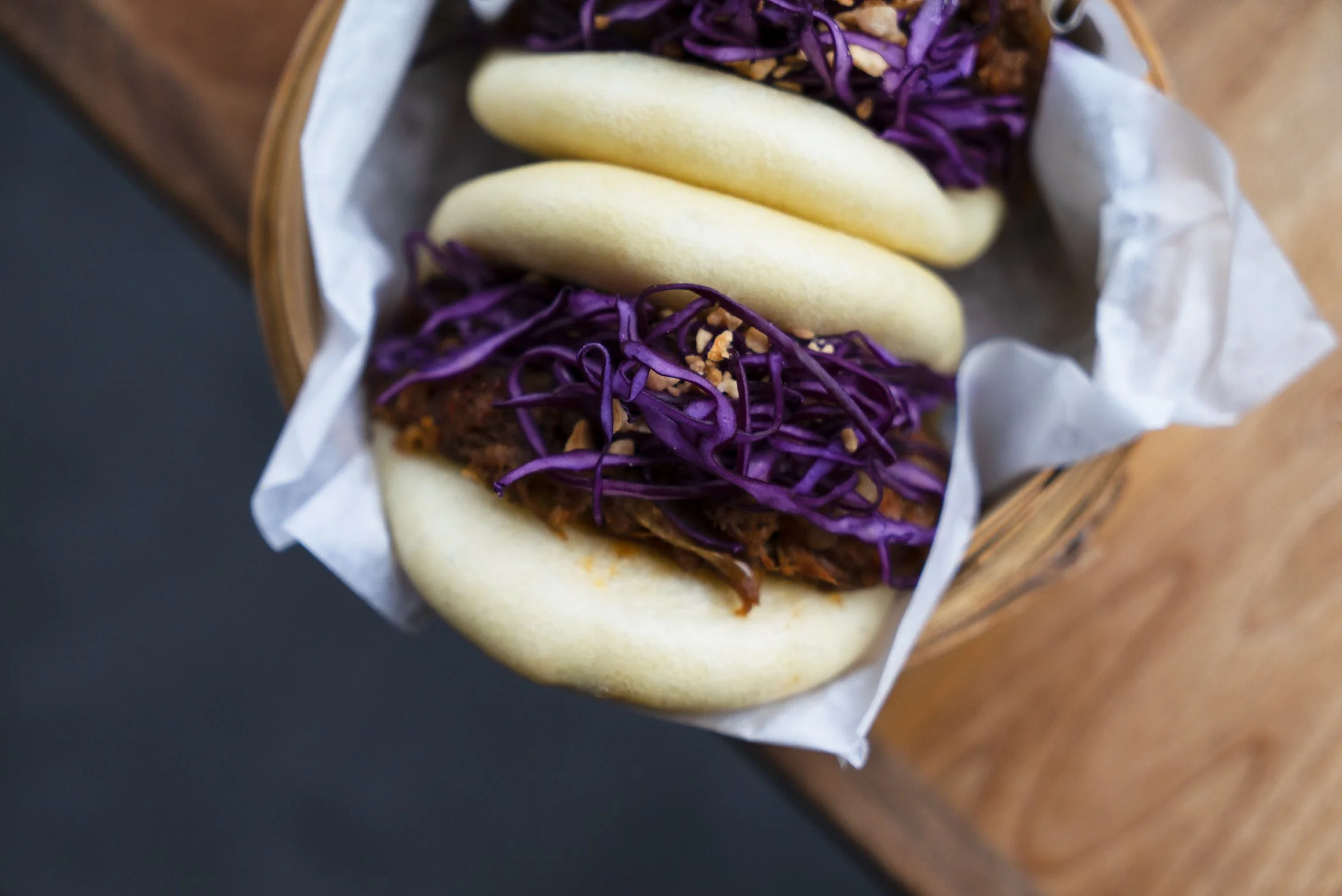 Bao topped with purple shredded cabbage and crushed nuts in a bun on a wooden table at Gongfu Bao. Photographed by Gumption Studio, Ottawa food photographer.