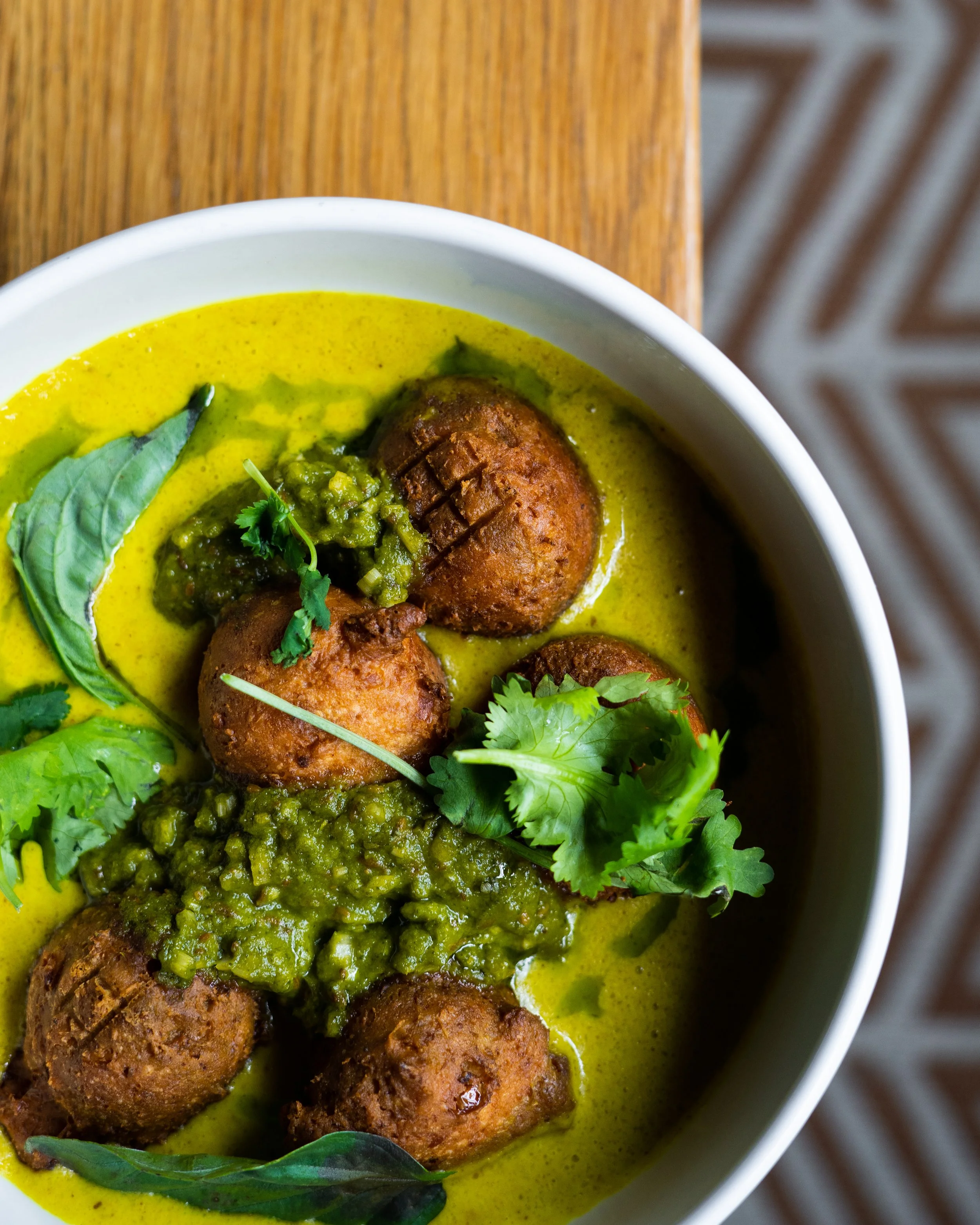 Close-up of a bowl of Thai curry from Sidedoor Restaurant garnished with green herbs on a wooden surface. Photographed by Gumption Studio, Ottawa food photographer.