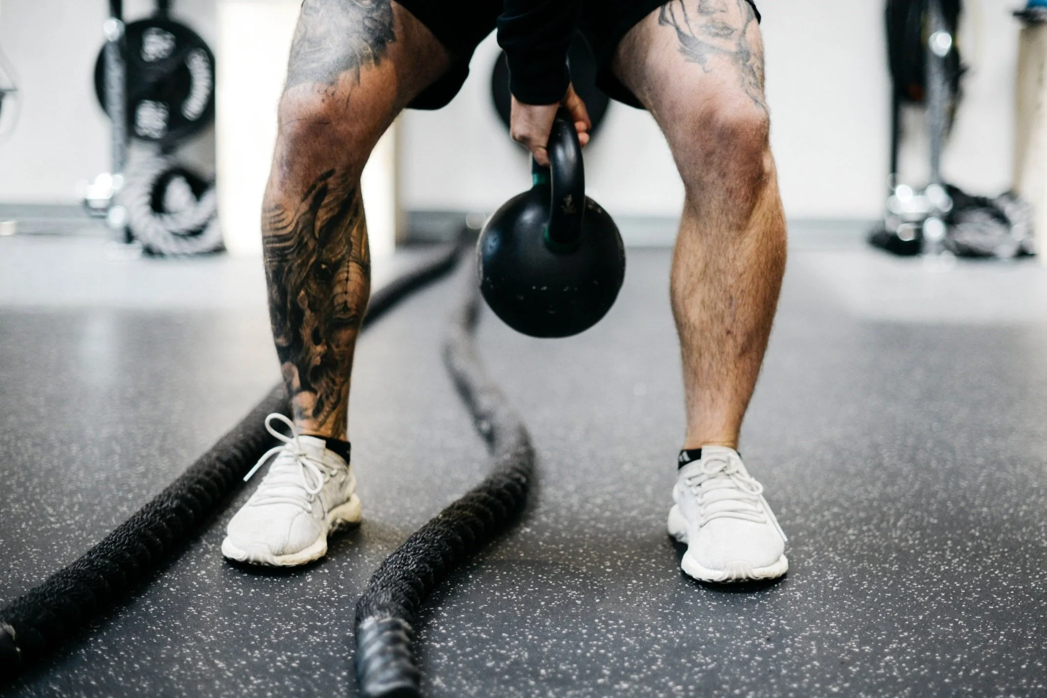 Person lifting a kettlebell in a gym, with battle ropes on the floor.