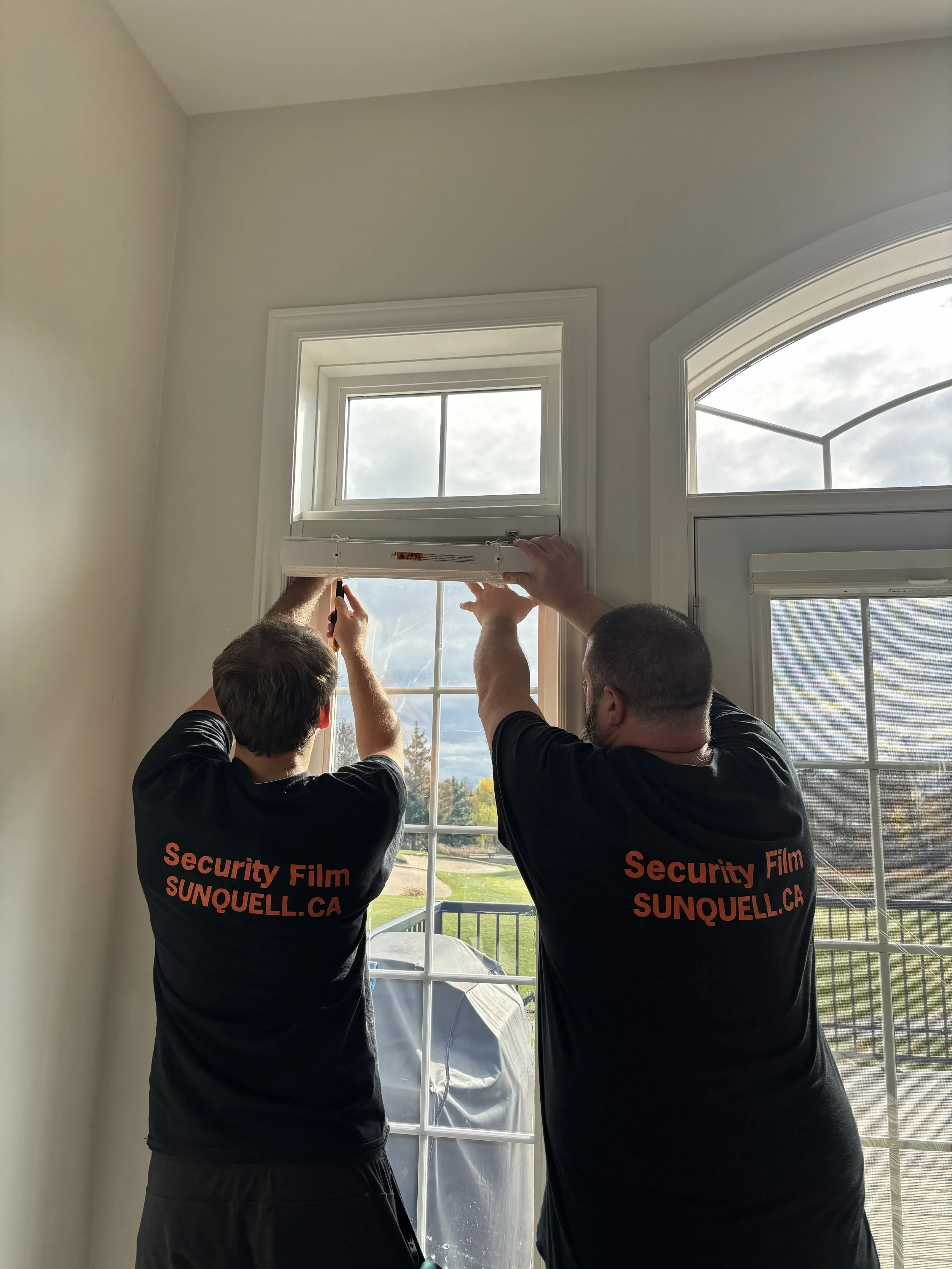 Professional installers applying window security film to a large glass door, reinforcing glass to help prevent break-ins and forced entry