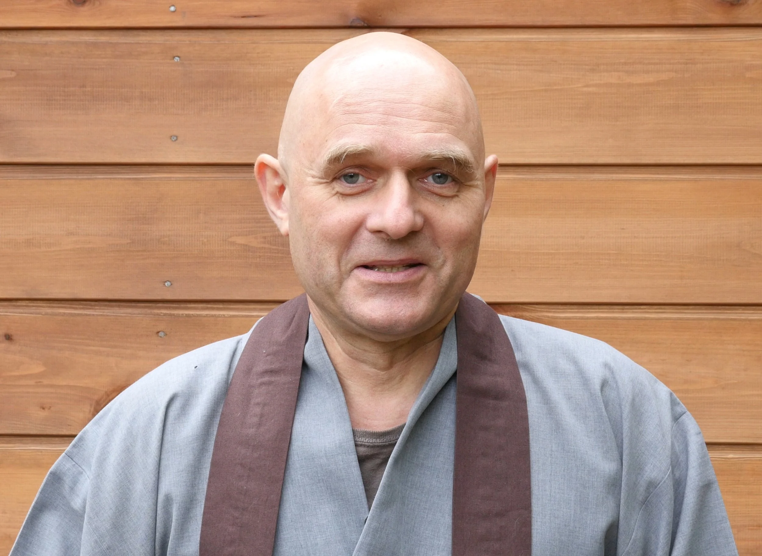 Igor smiles at the camera before a wooden wall