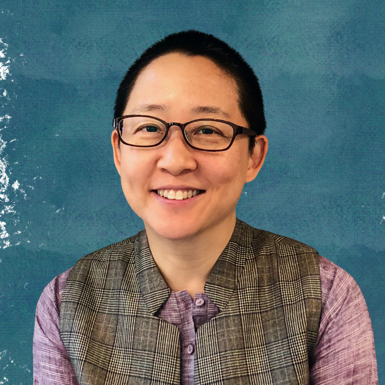 Kathy smiles in glasses and a vest, before a blue background