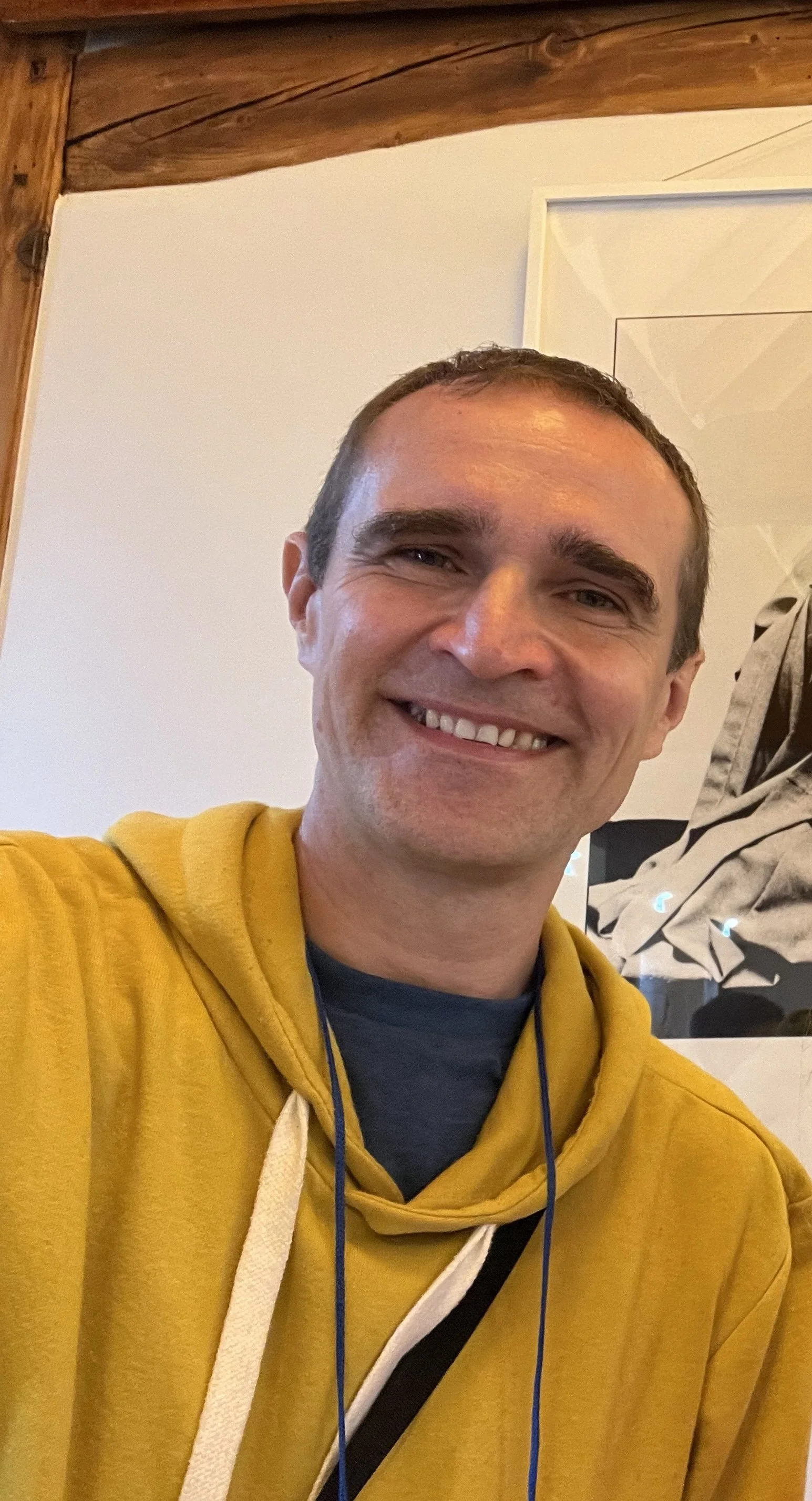 Dusan smiles at the camera wearing a mustard yellow hoodie