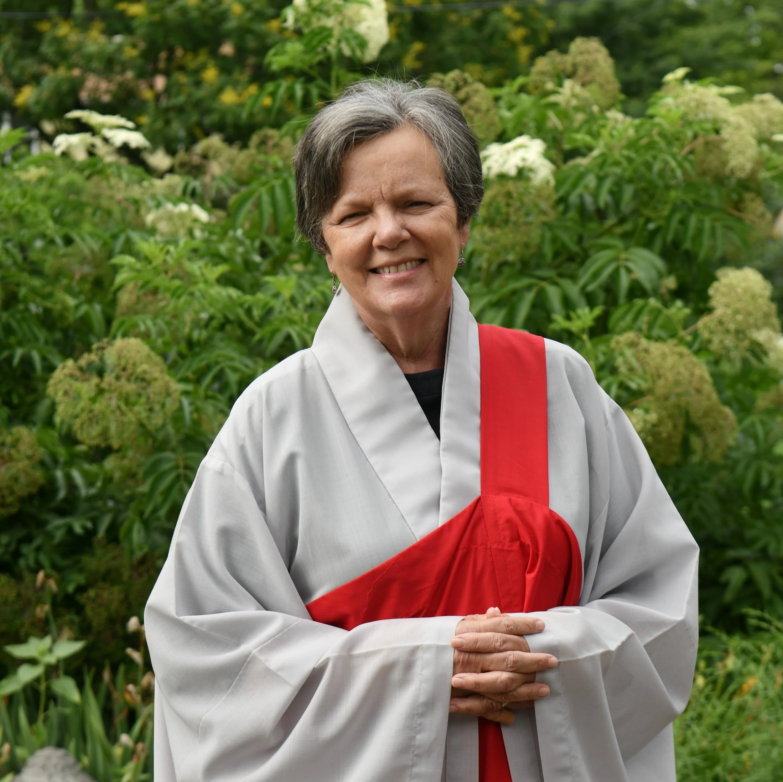 Rebecca stands in a garden with her hands folded
