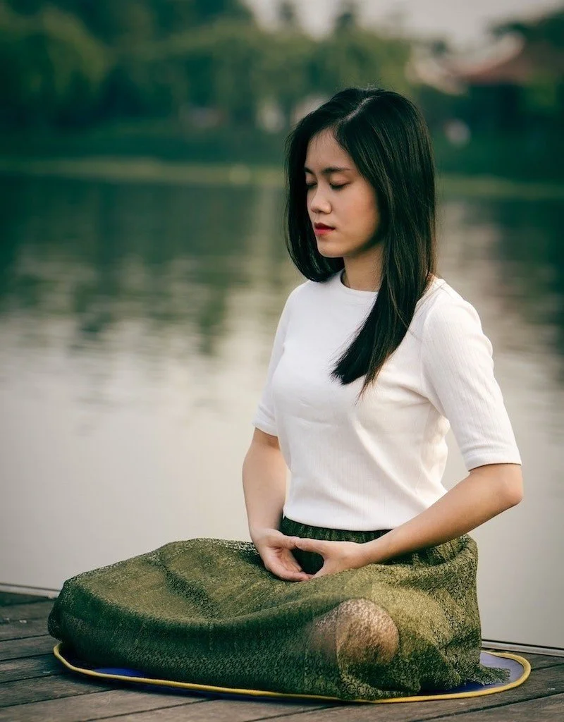 An asian woman sits outside and meditates