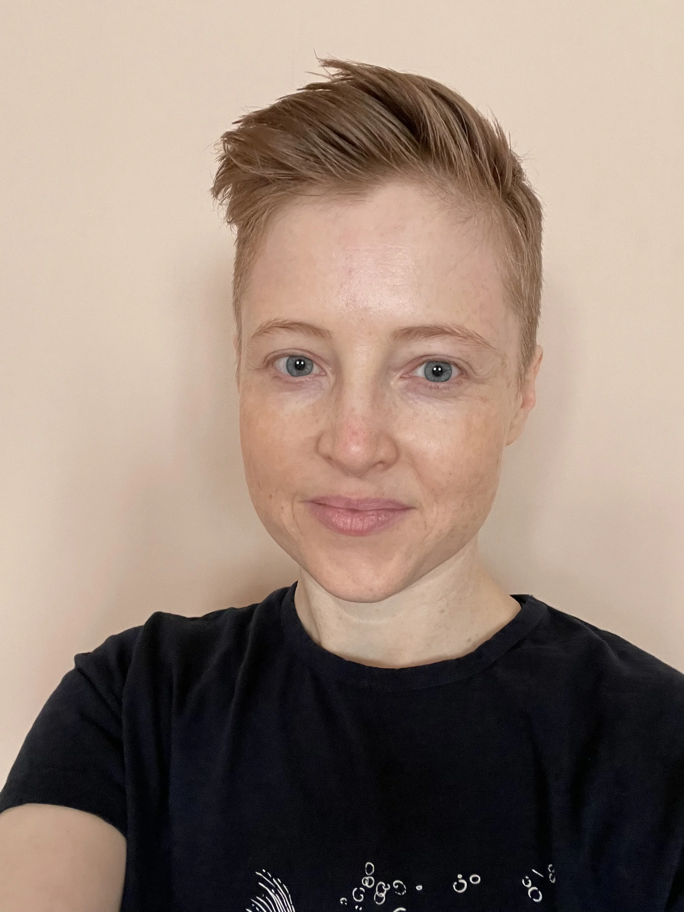 Tam stands in a T-shirt before a white wall