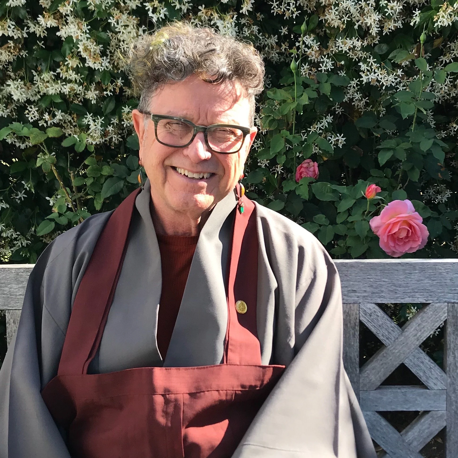 Tim sits on a park bench and smiles to the camera