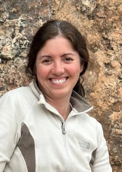 Barbara smiles in a two-toned zip up, in front of a rock