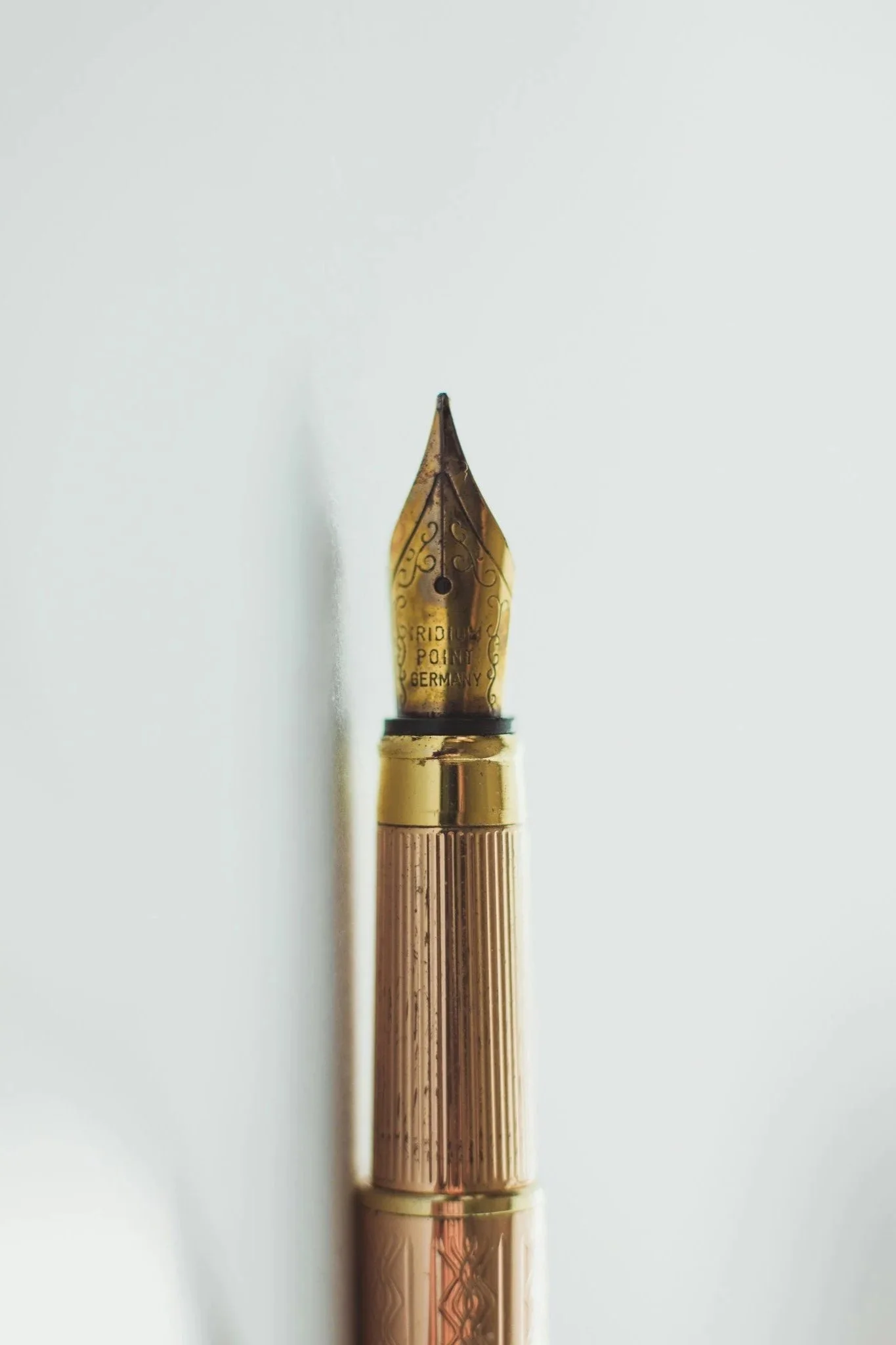 Close-up photo of a gold fountain pen nib with intricate engravings, marked with 'IRIDIUM POINT GERMANY', resting against a white background.