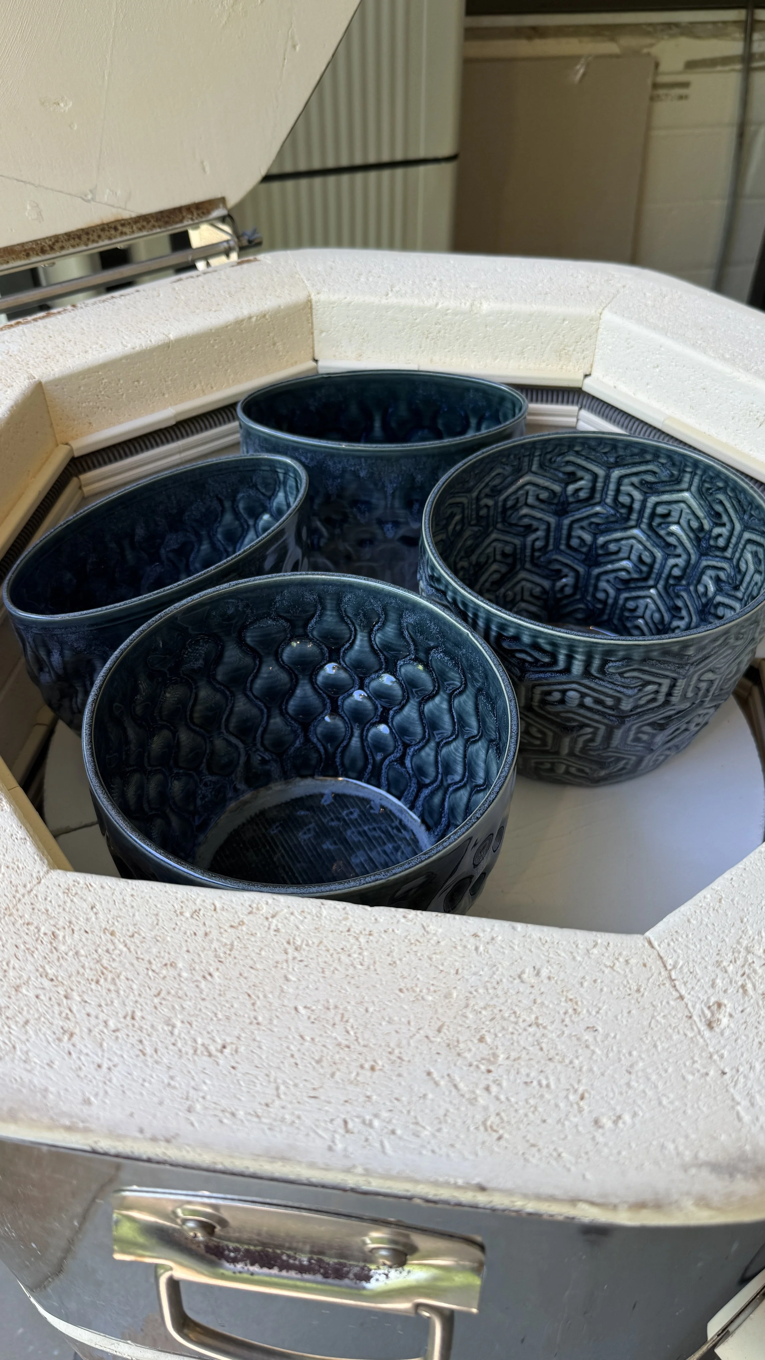 Four dark blue ceramic vases and planters with intricate patterns placed inside a kiln for post firing.