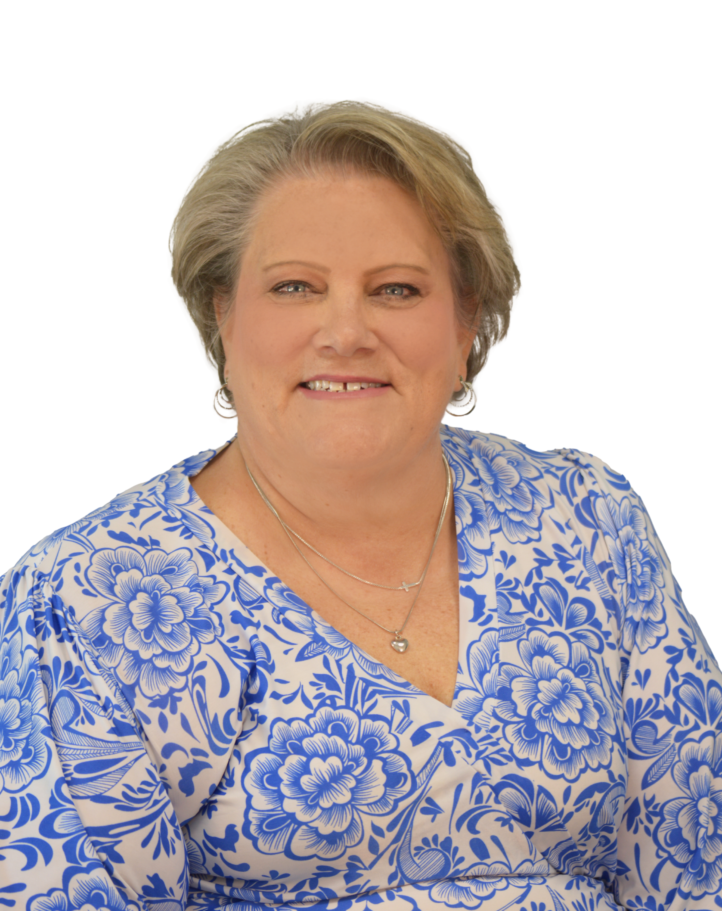 A woman with short gray hair wearing a blue and white floral patterned dress and layered necklaces.