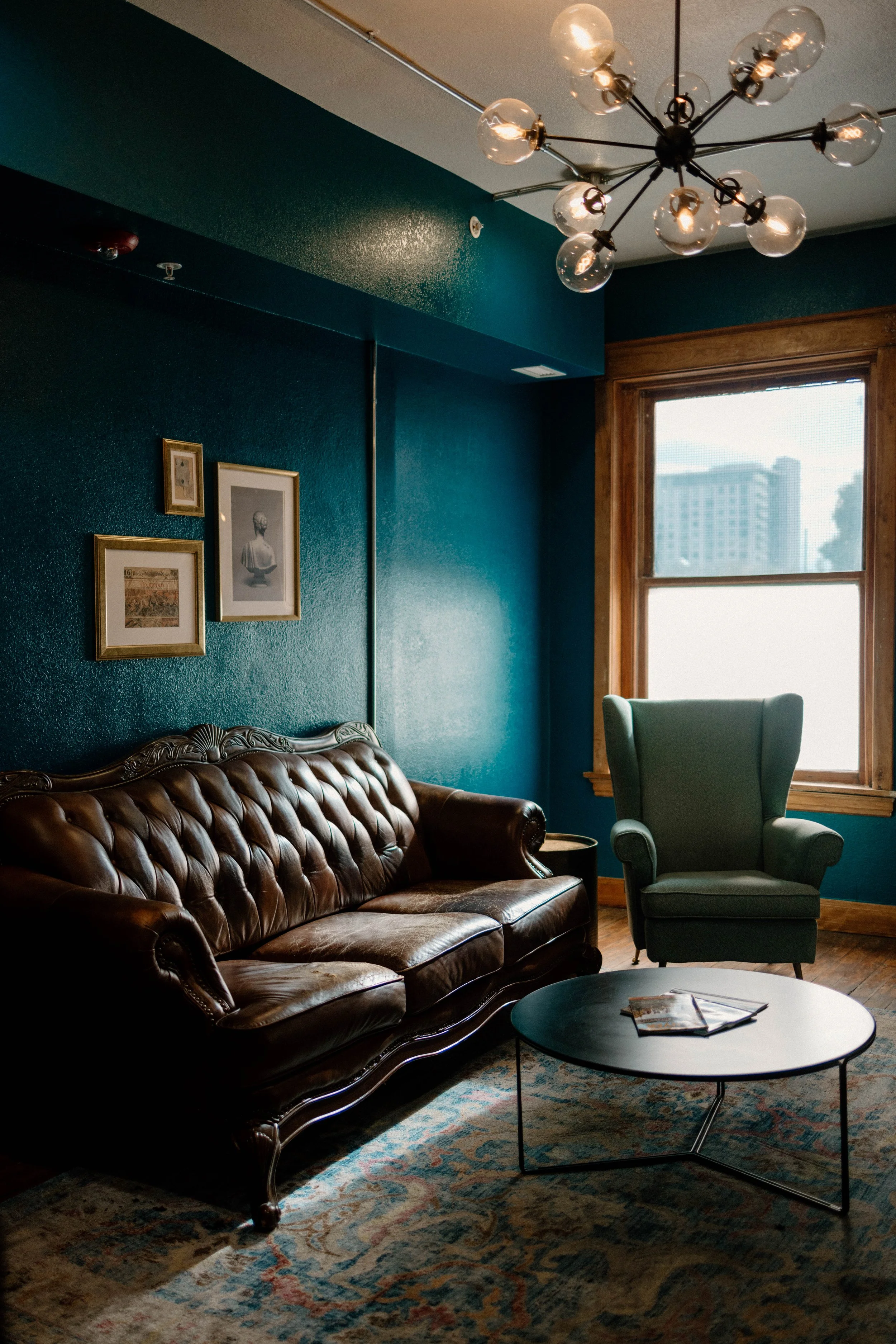 A dark brown leather sofa in a teal-colored room next to a circular coffee table and a green armchair.