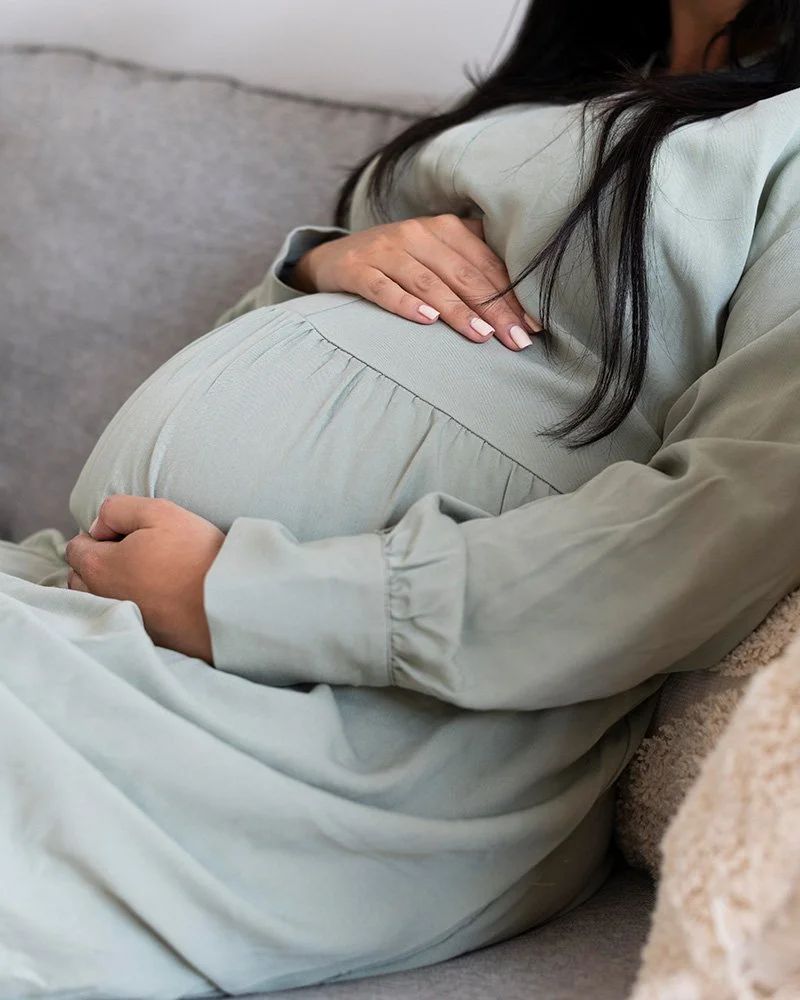 Pregnant person sitting on a bed, cradling their baby bump with both hands