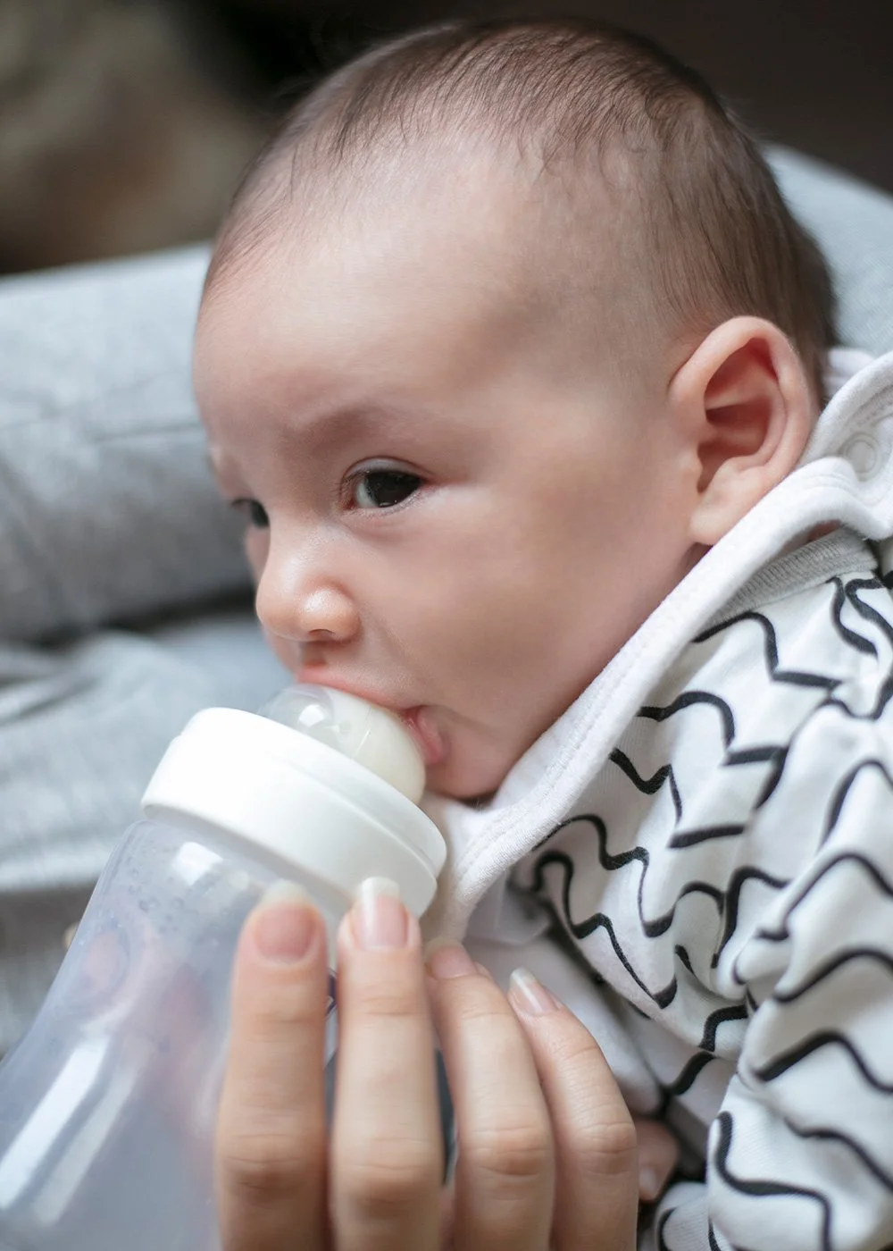 Baby drinking from a bottle while looking up with bright eyes