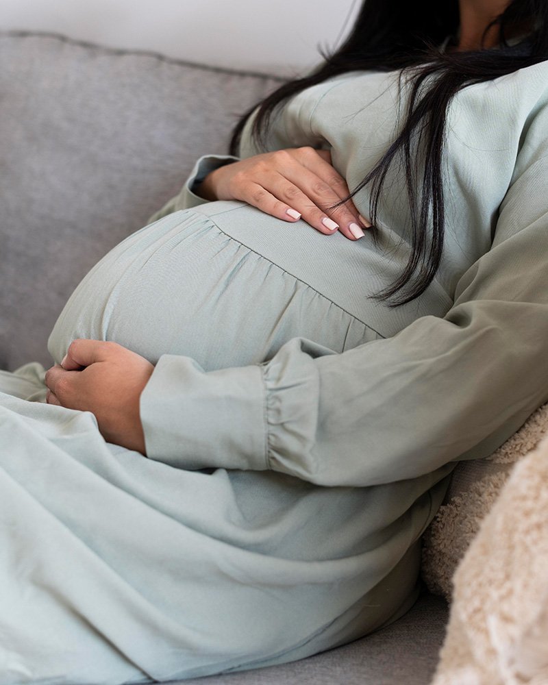 Pregnant person sitting on a couch, gently cradling their belly