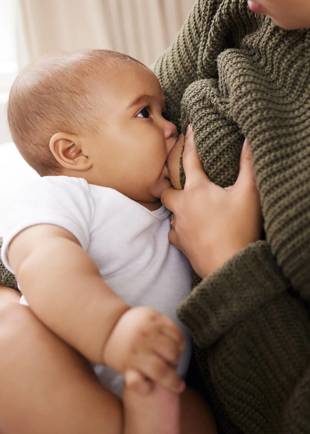 Baby breastfeeding while a parent gently lifts their knit sweater to nurse