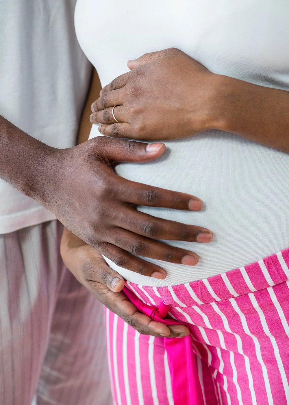 Close-up of a pregnant person’s belly with her partner's hand gently resting on the belly