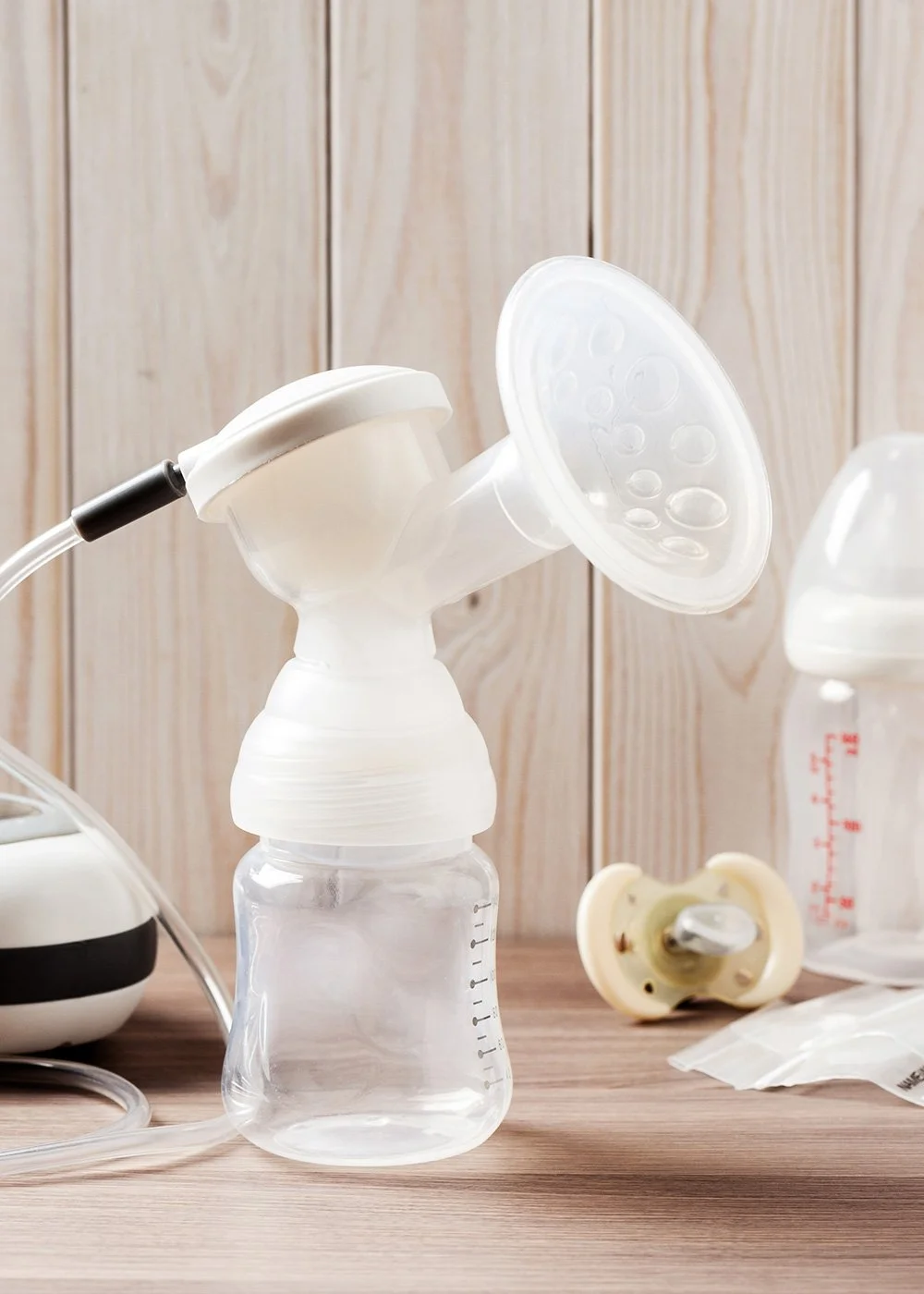 Close-up of a breast pump on a table beside a pacifier and bottle
