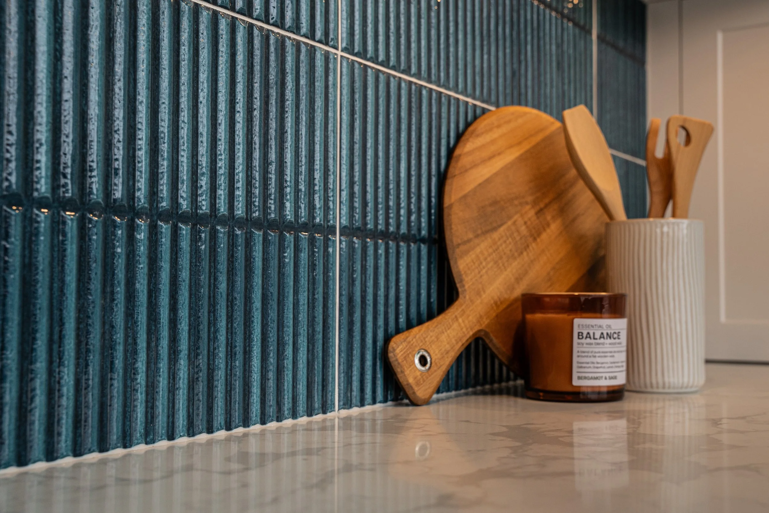 Close-up of a blue textured wall behind a wooden decorative object and a ceramic container, positioned on a marble countertop.