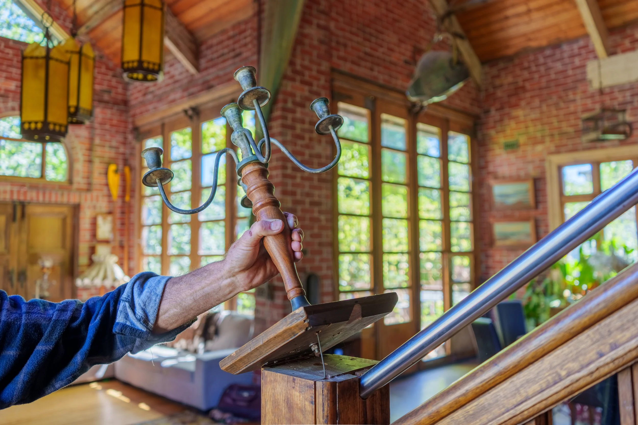 A person holding an antique candelabrum with three candle holders in a bright, rustic room with wooden and brick elements.