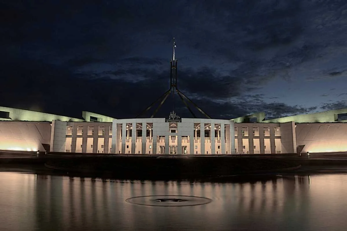 Nighttime view of the Australian Parliament House in Canberra, illuminated with its reflection on a water feature in front.