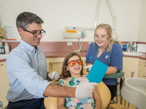 Arena Dental dentist and assistant helping a young patient during a check-up in a friendly dental clinic.