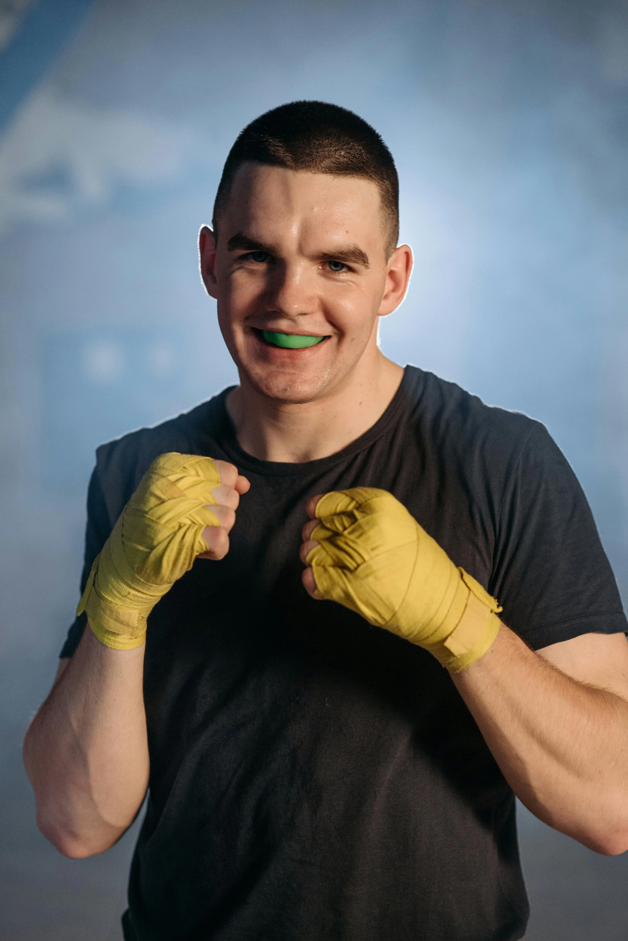 Man wearing a green mouthguard holding his wrapped hands up in a boxing position