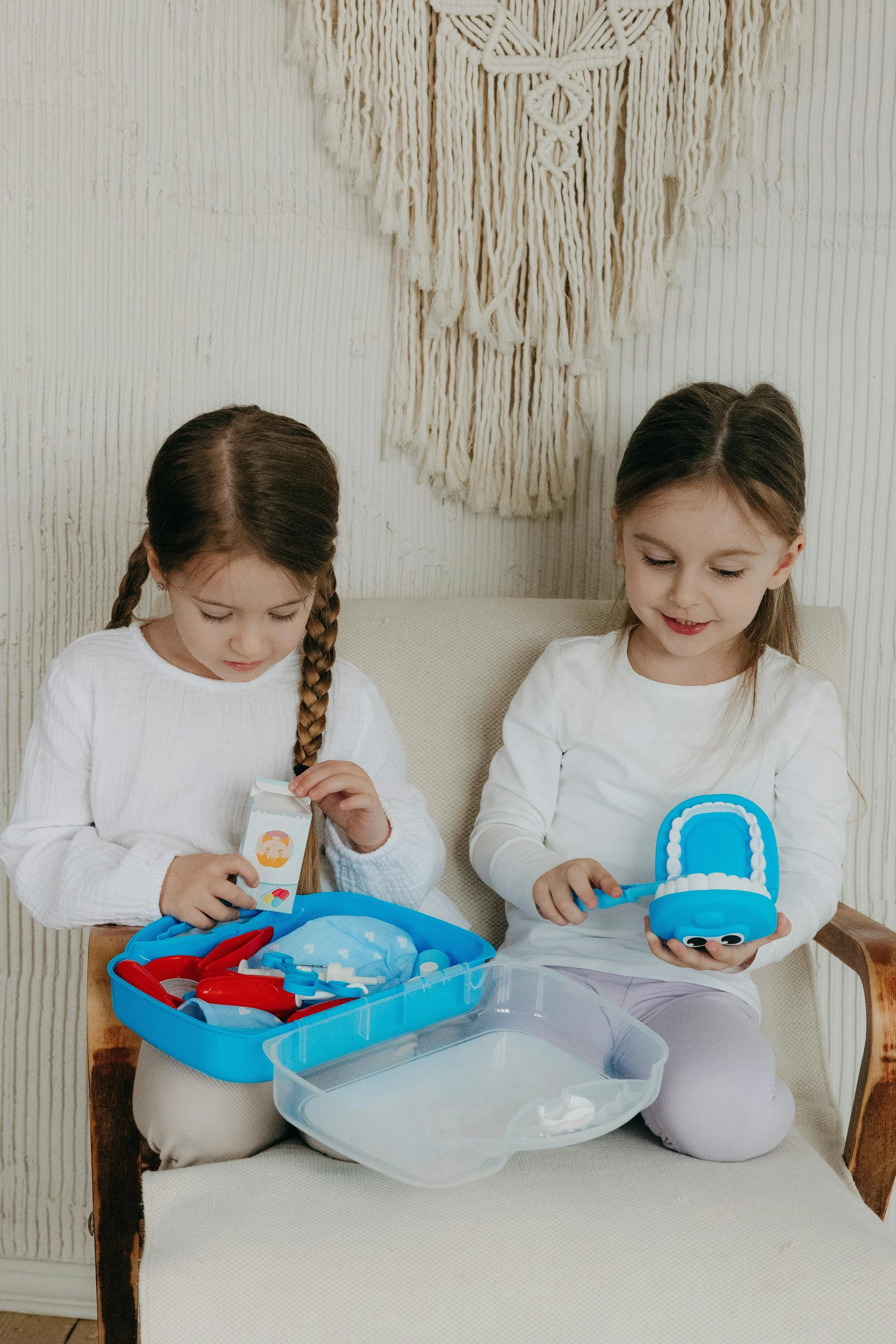Two young girls learning about dental care with toy dentist kit and teeth model.