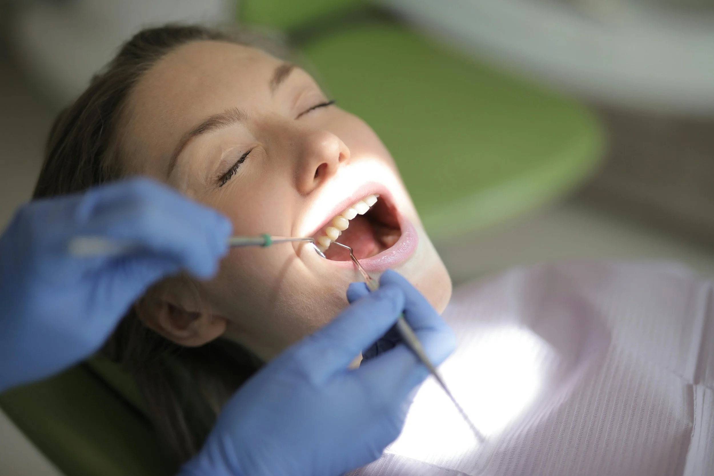 Dentist with blue gloves examining patient’s teeth during appointment