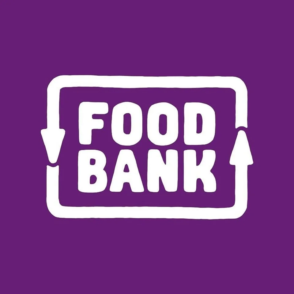 Logo of a food bank with a purple background and white text reading 'Food Bank' inside a rectangular outline with arrows.