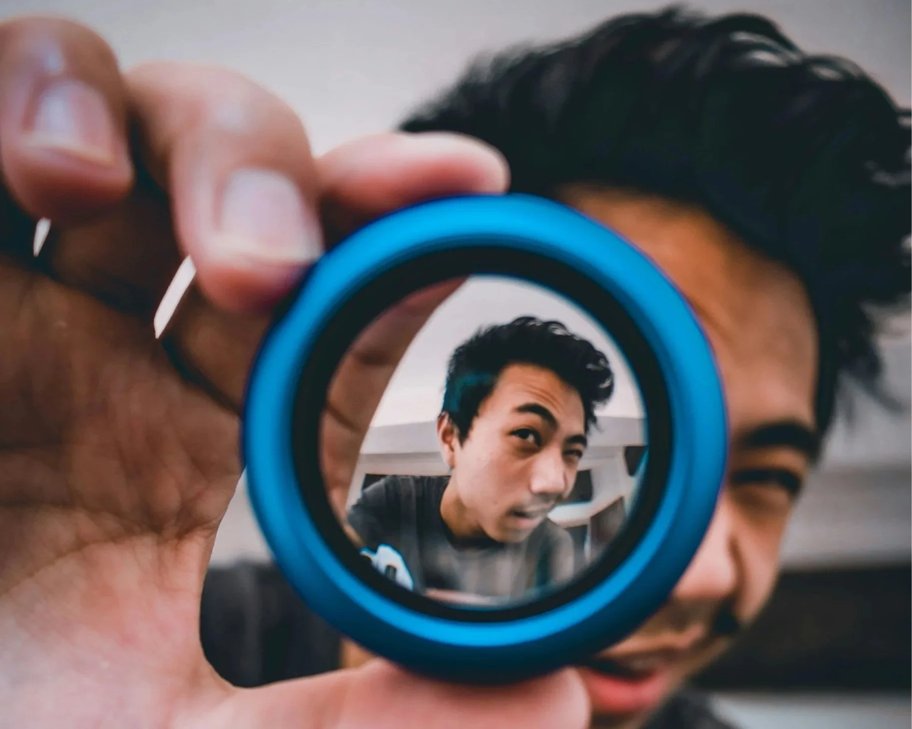 Person holding a camera lens in front of a mirror, capturing their reflection.