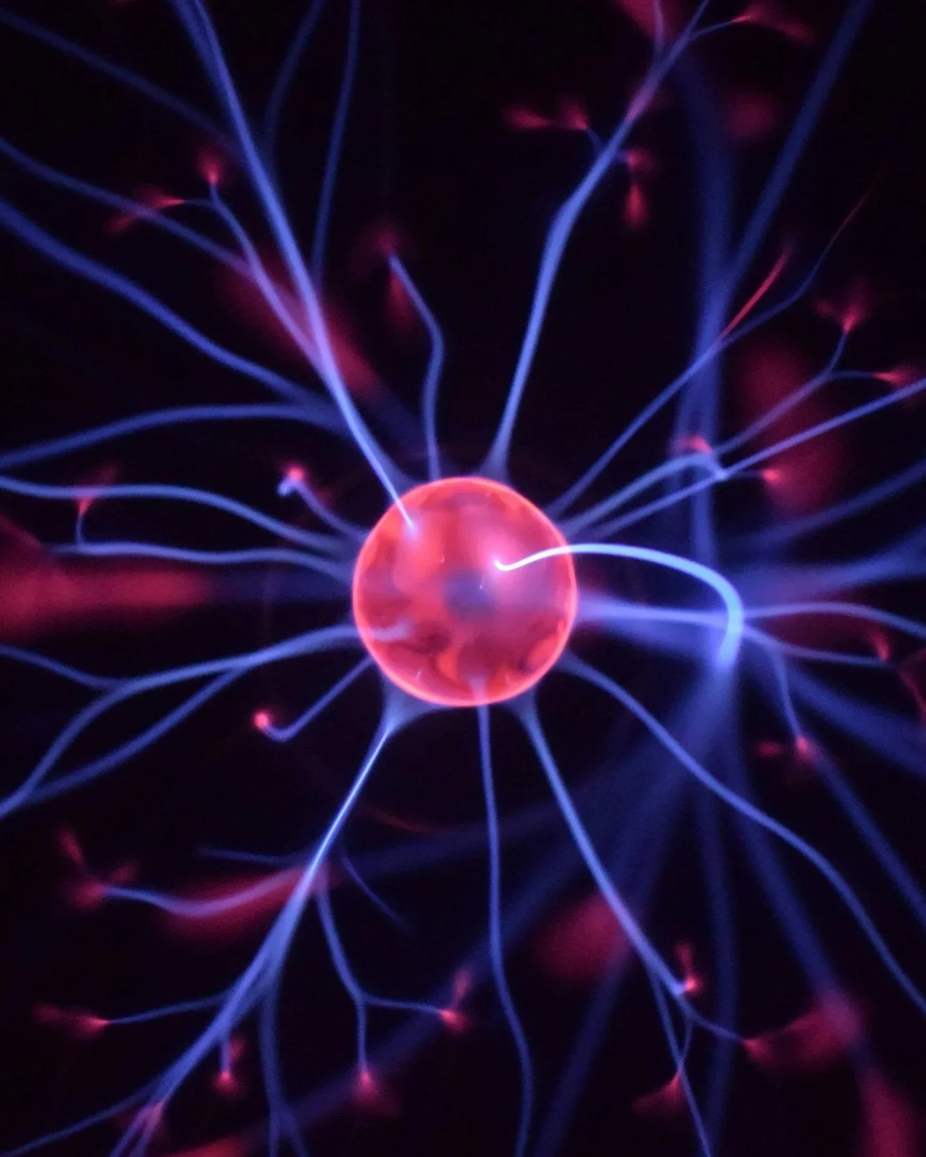 Brightly colored plasma ball with electric tendrils radiating outward in purple and blue against a black background.