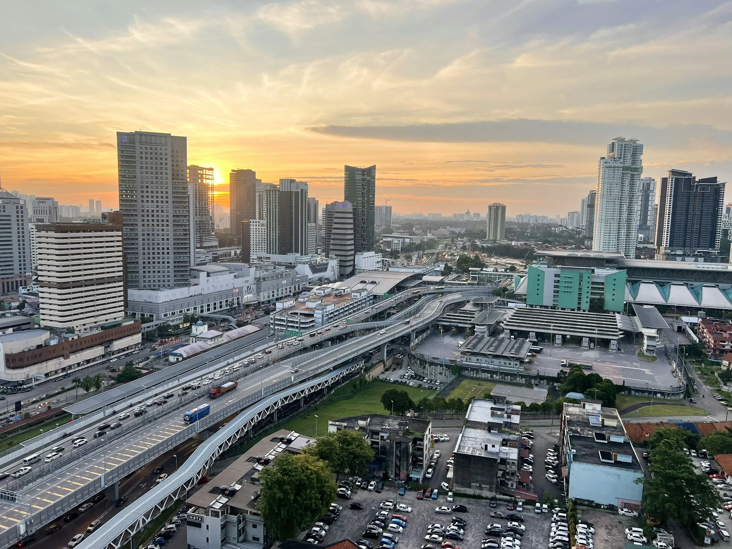 City skyline at sunset with tall buildings, highways, and parking lots.