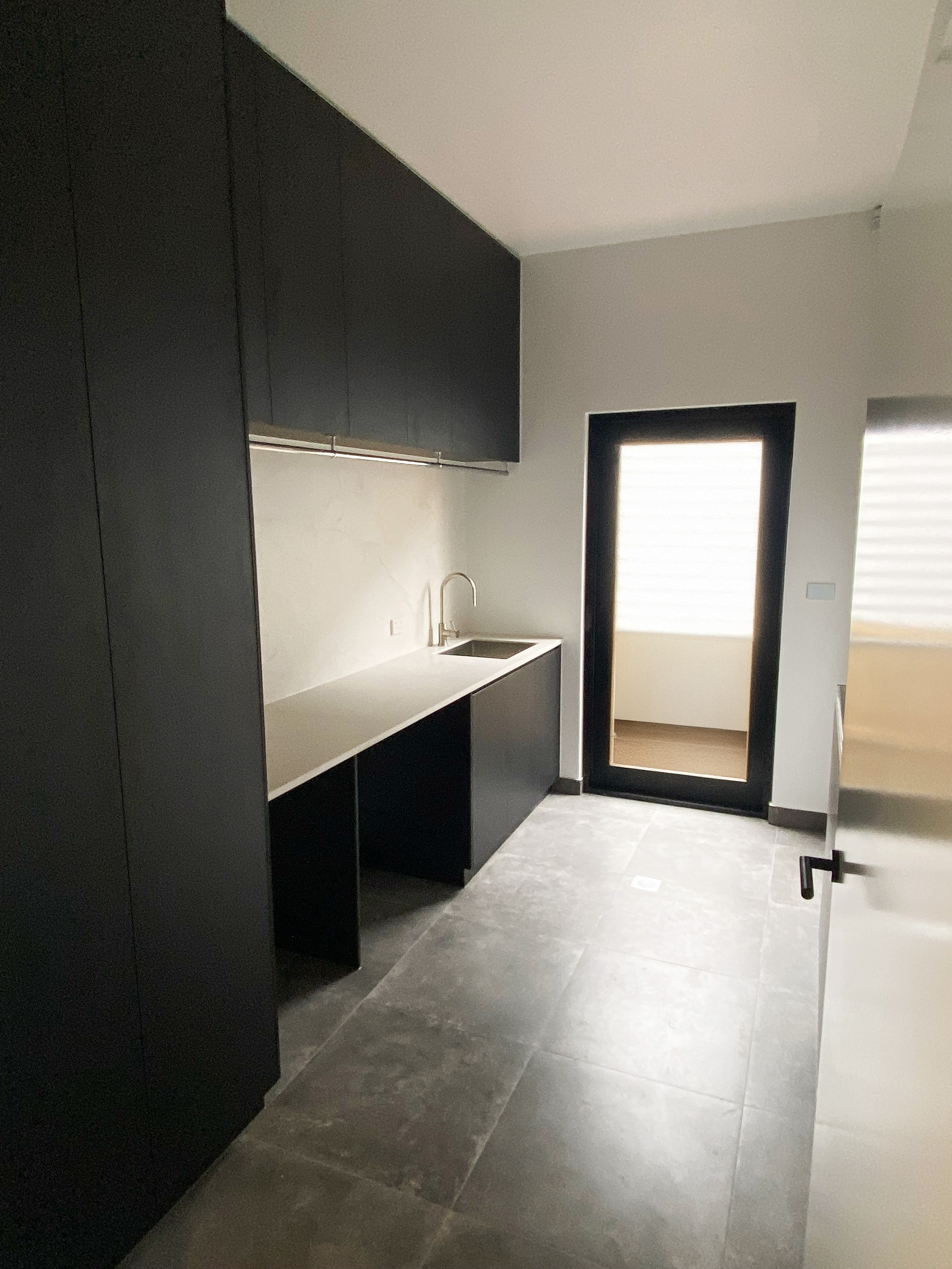 Modern kitchen with black cabinets, white countertop, stainless steel sink with faucet, and a door with window blinds.