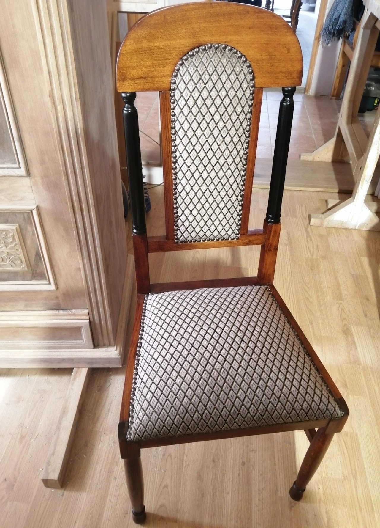 Wooden dining chair with patterned upholstery on the seat and backrest, placed on a wooden floor next to a wooden cabinet.