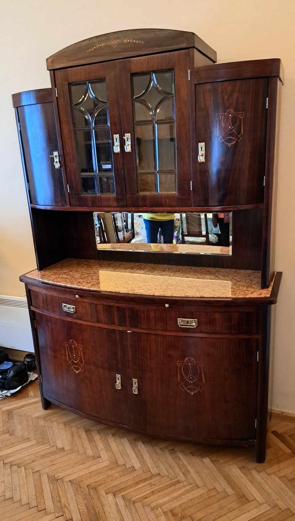 Vintage wooden secretary desk with glass-front upper cabinet and mirror, set against a beige wall on a hardwood floor.