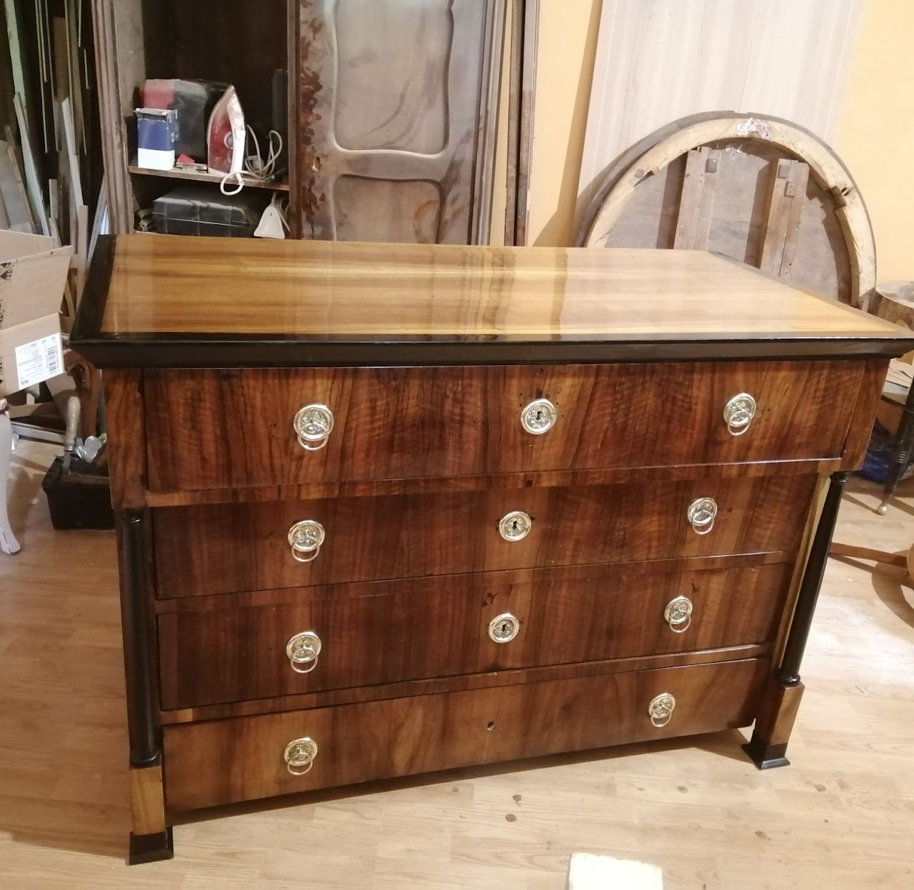 A vintage wooden dresser with a polished top, five drawers with round metallic handles, and black metal legs.
