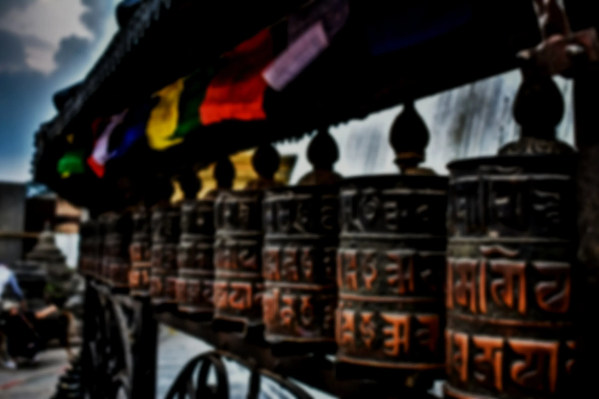 A row of traditional Tibetan prayer wheels with colorful prayer flags above them.