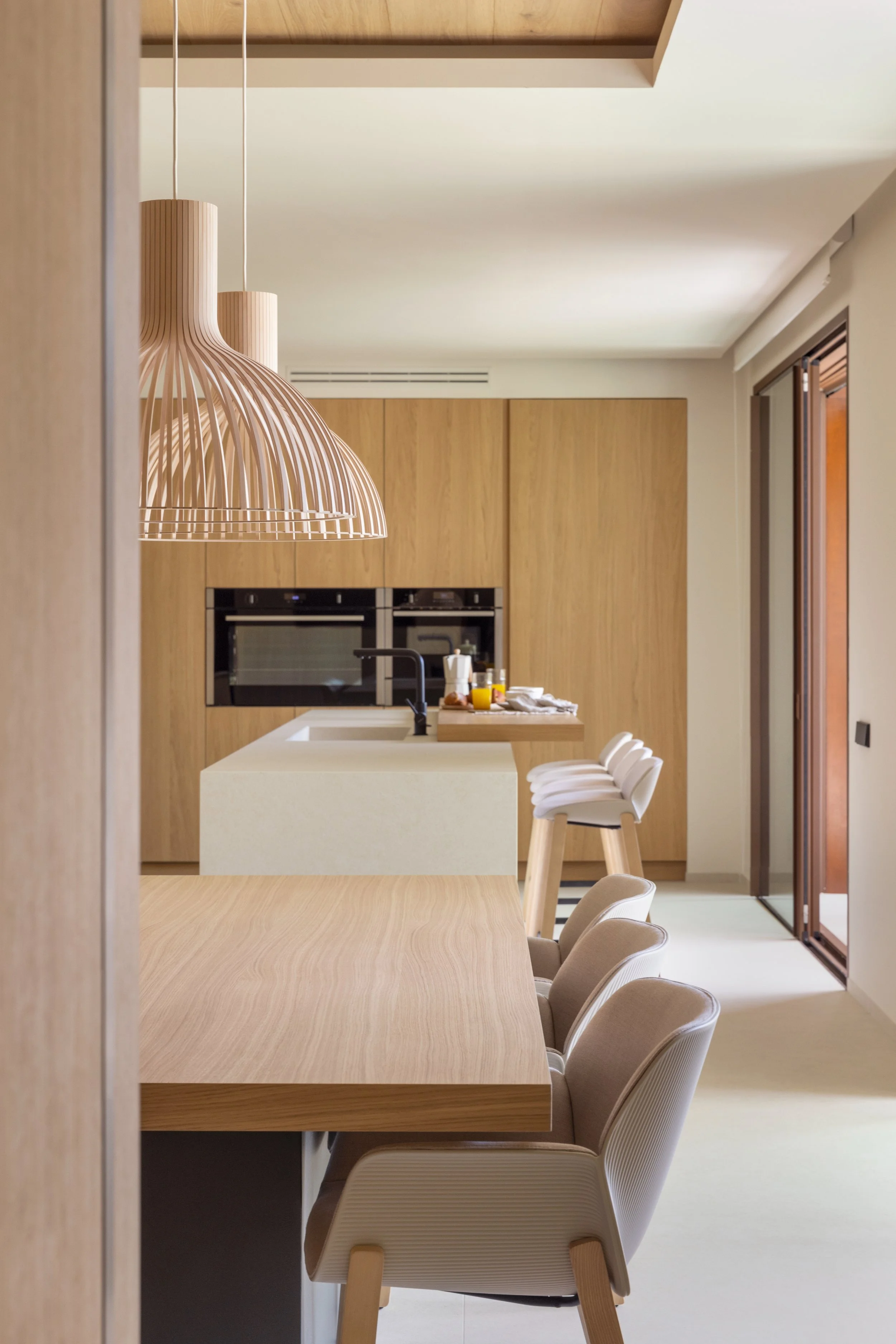 Modern kitchen and dining area with wood cabinetry, light-colored chairs, and minimalist design.