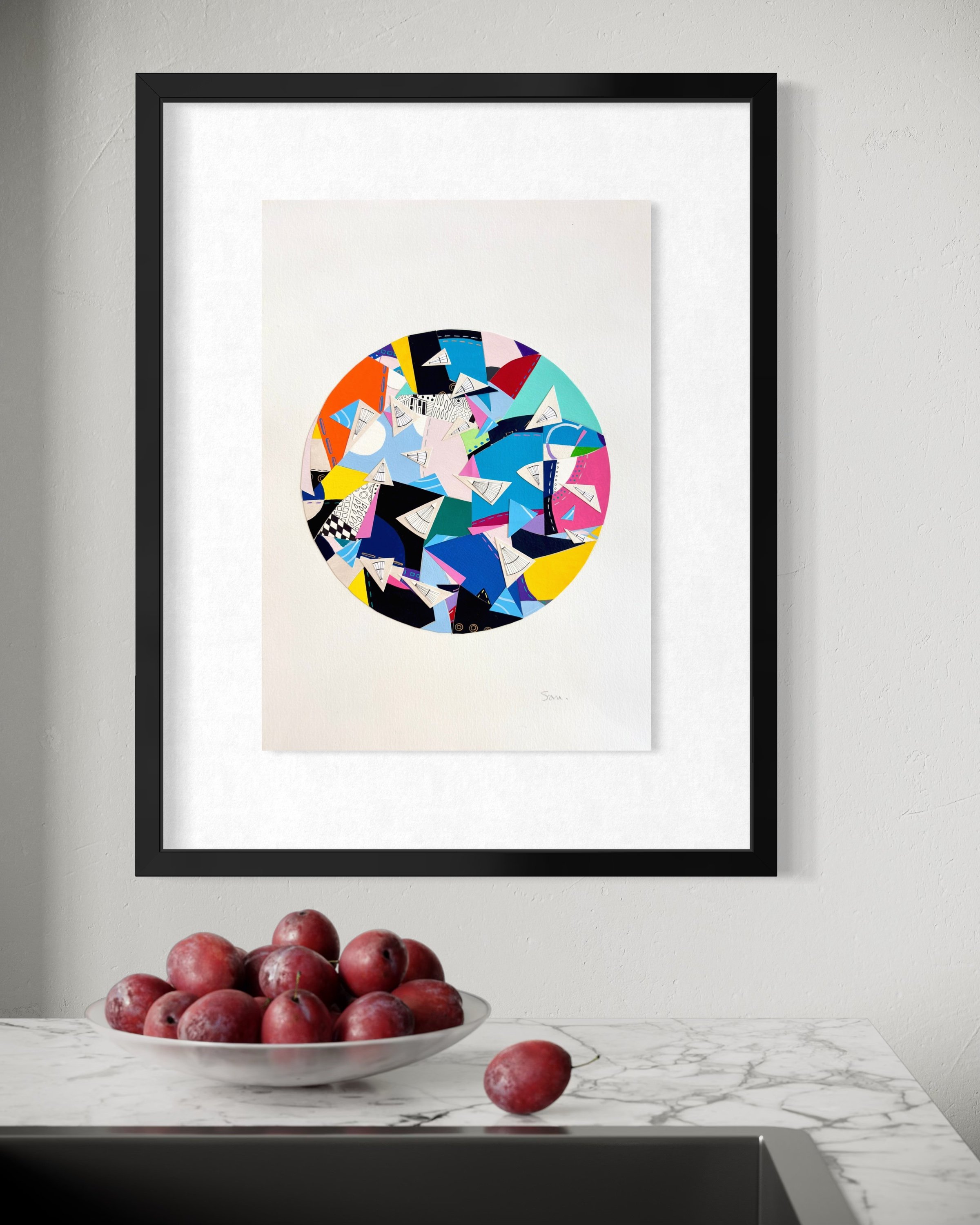 A Restless Centre, A3 abstract mixed media collage with a circular centre of coloured fragments and triangular pen drawings displayed framed above a stone bench top.
