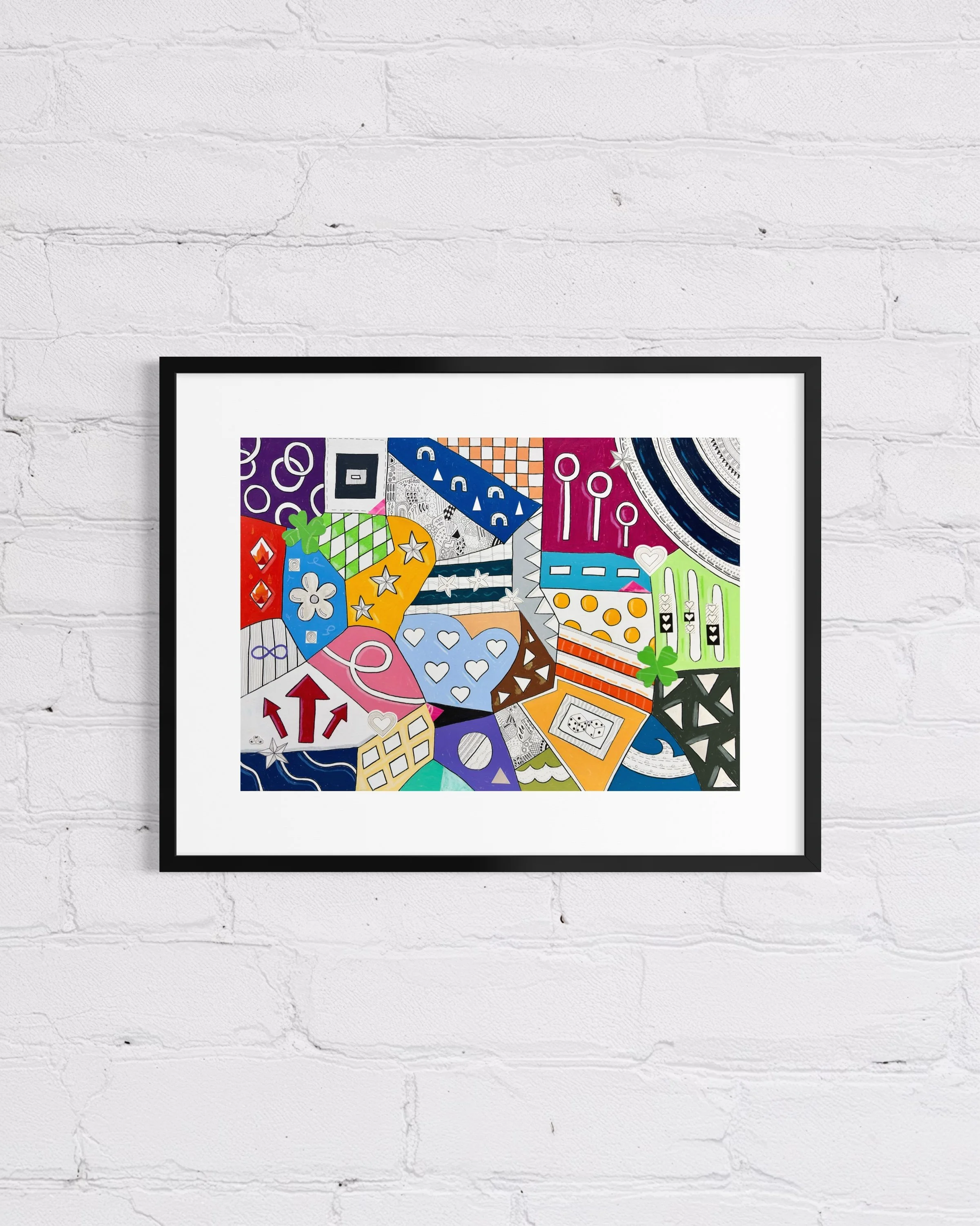 A2 mixed media artwork on paper titled Devotion and Chance, colourful abstract composition with hearts, swans, flames, dice, clovers, stars, and horseshoes, framed and displayed on a white brick wall.