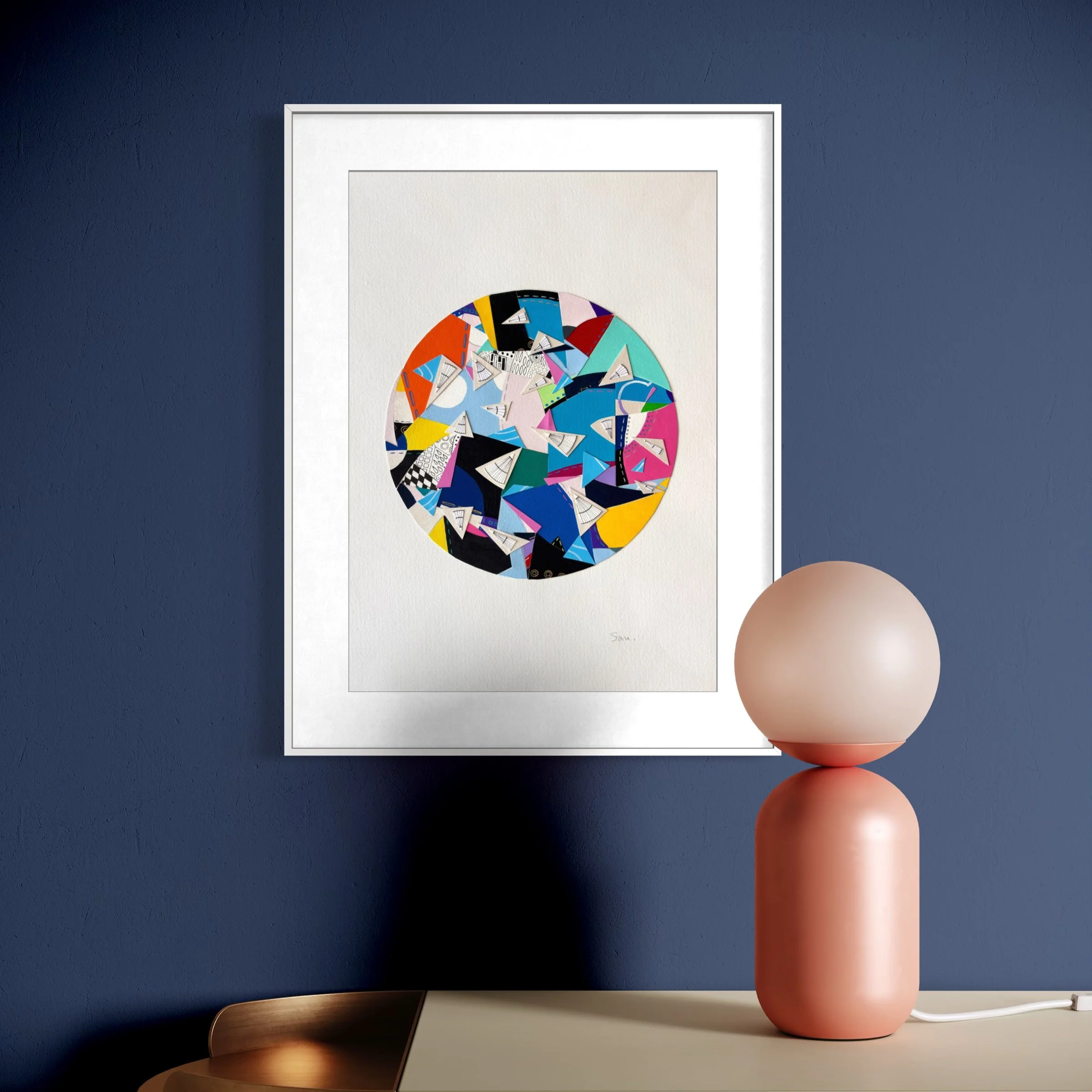 A Restless Centre, A3 abstract mixed media collage with a circular centre of coloured fragments and triangular pen drawings displayed framed above a table.