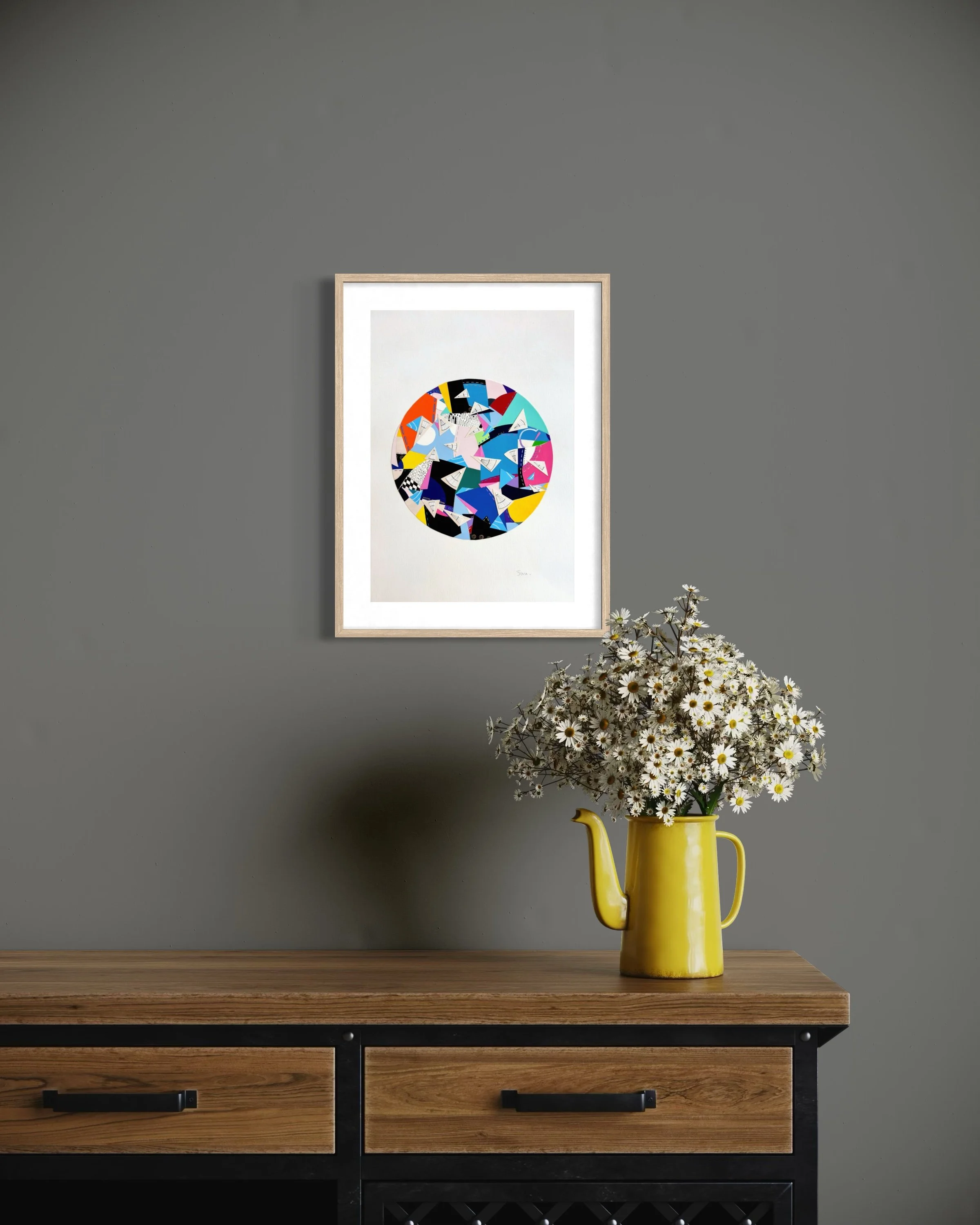 A Restless Centre, A3 abstract mixed media collage with a circular centre of coloured fragments and triangular pen drawings displayed framed above a hallway table.