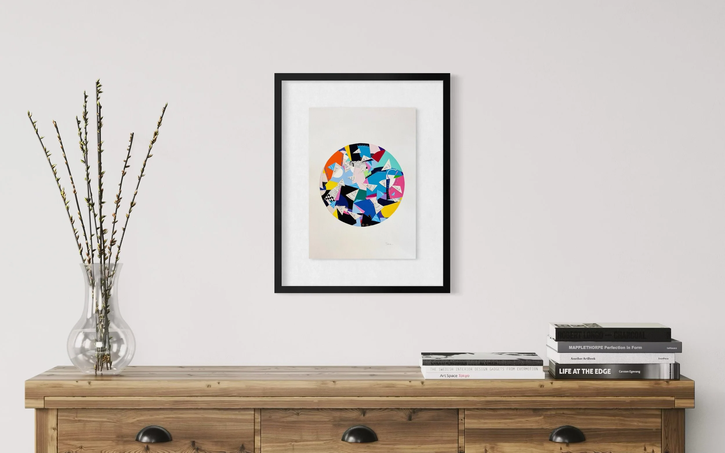 A Restless Centre, A3 abstract mixed media collage with a circular centre of coloured fragments and triangular pen drawings displayed framed above a wooden chest of drawers.