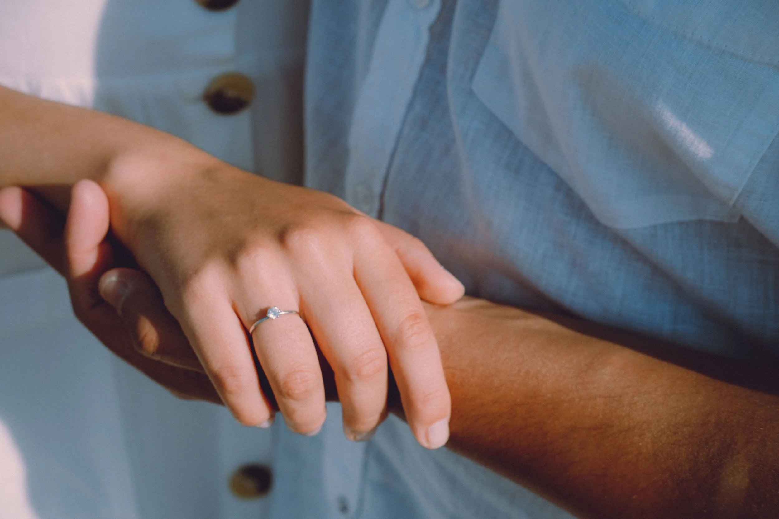 Eine Hand mit einem Ring legt auf den Unterarm einer anderen Person.